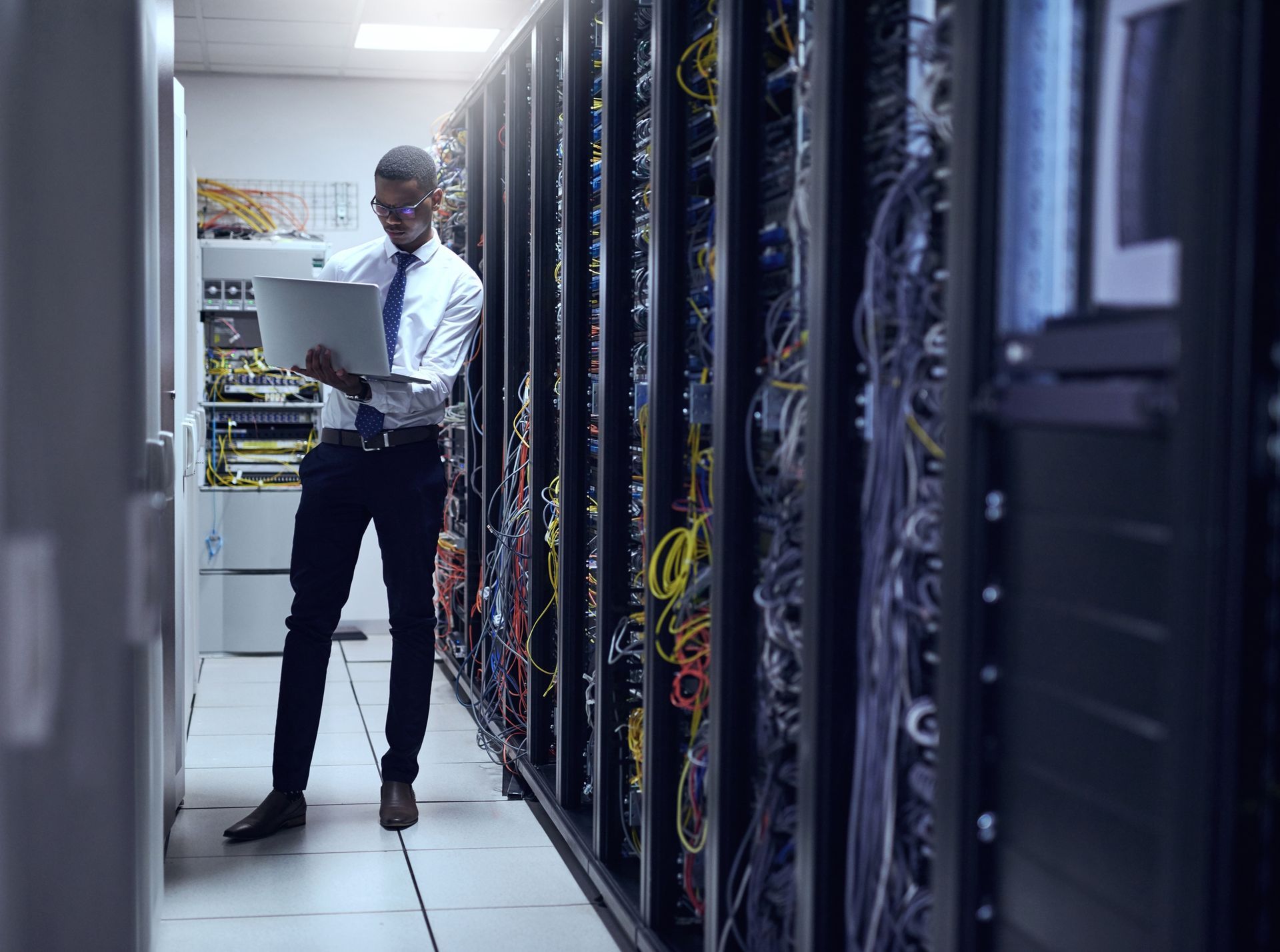 A man is using a laptop in a server room.