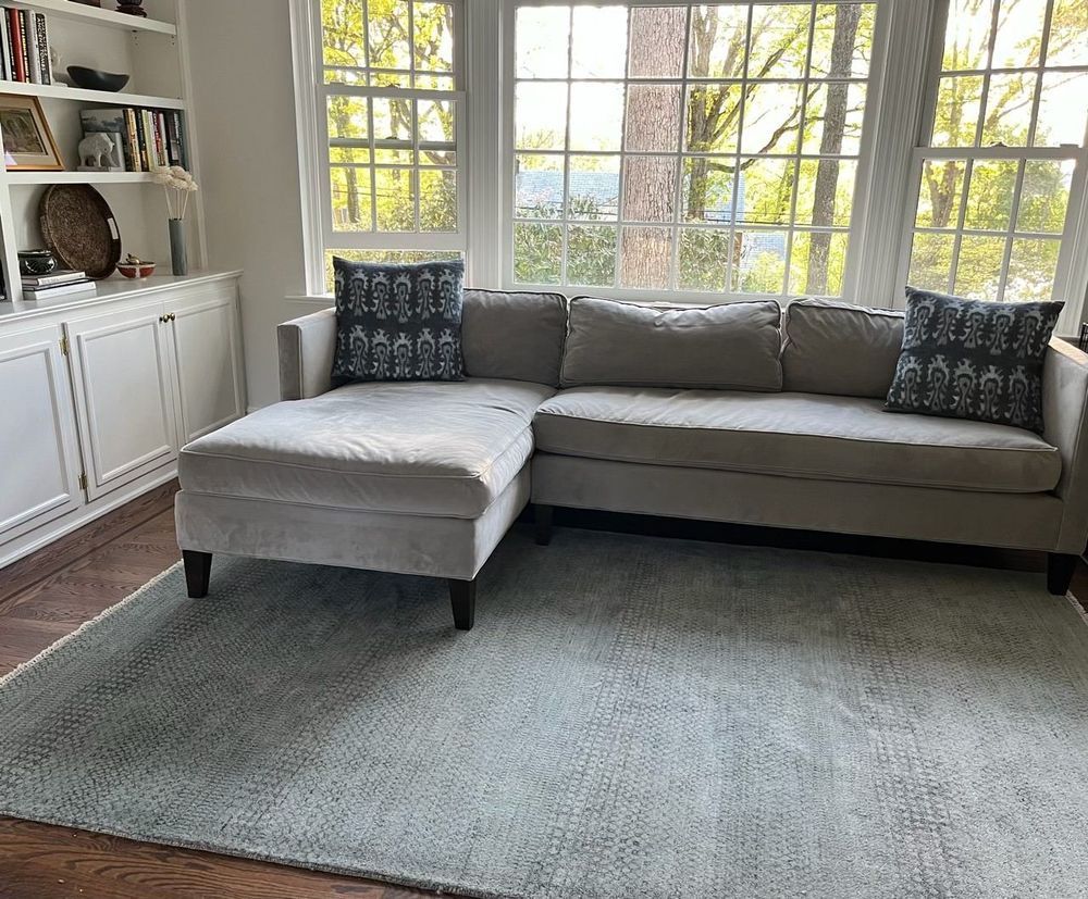 A living room with a sectional couch and ottoman in front of a window.