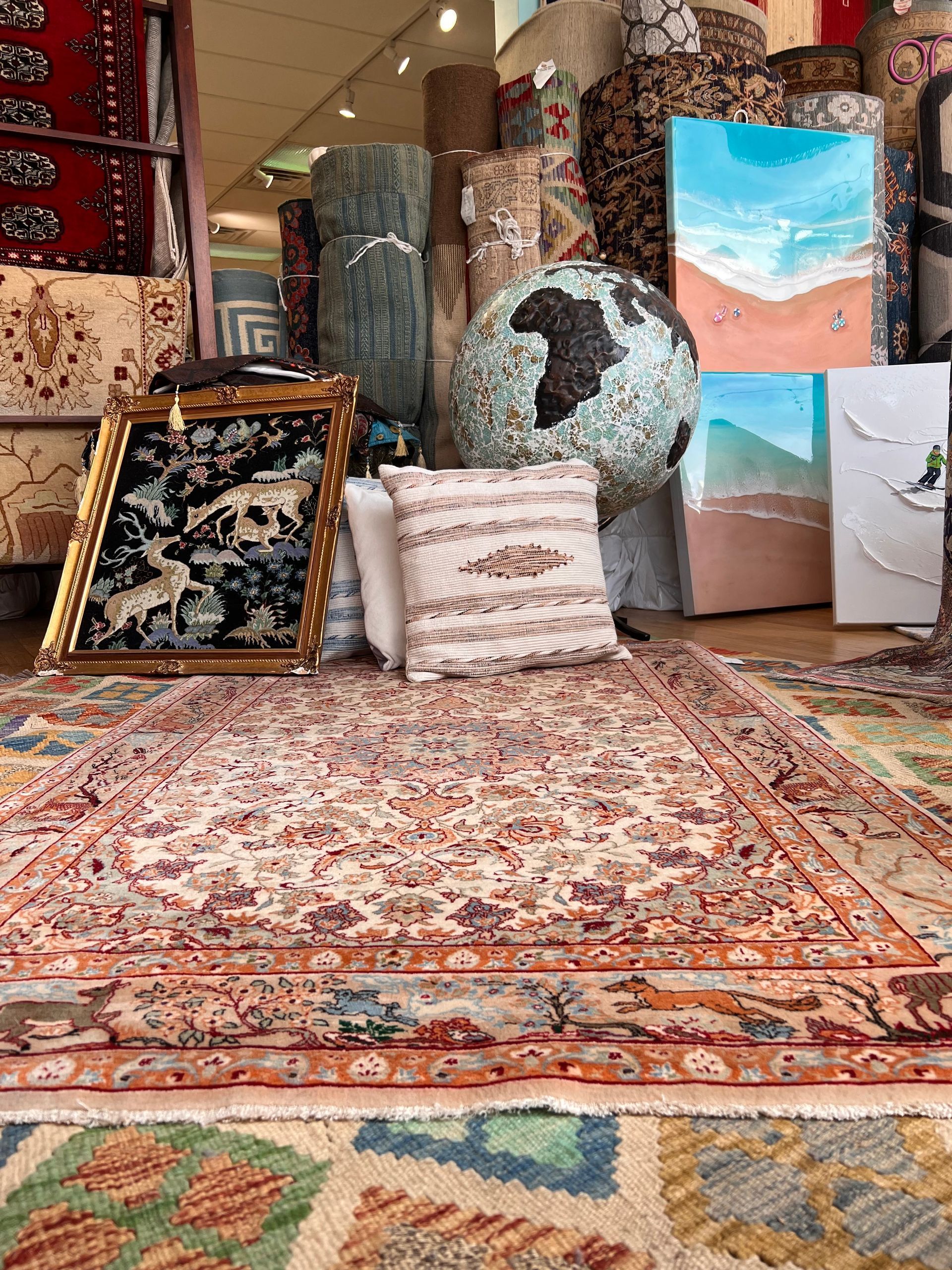 A room with a rug , pillows , and paintings on the floor.