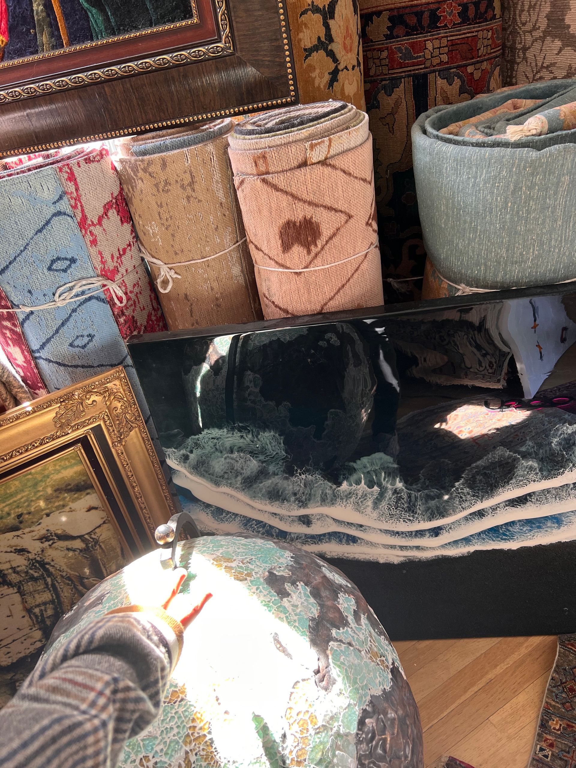 A person is standing in front of a pile of rugs and paintings.