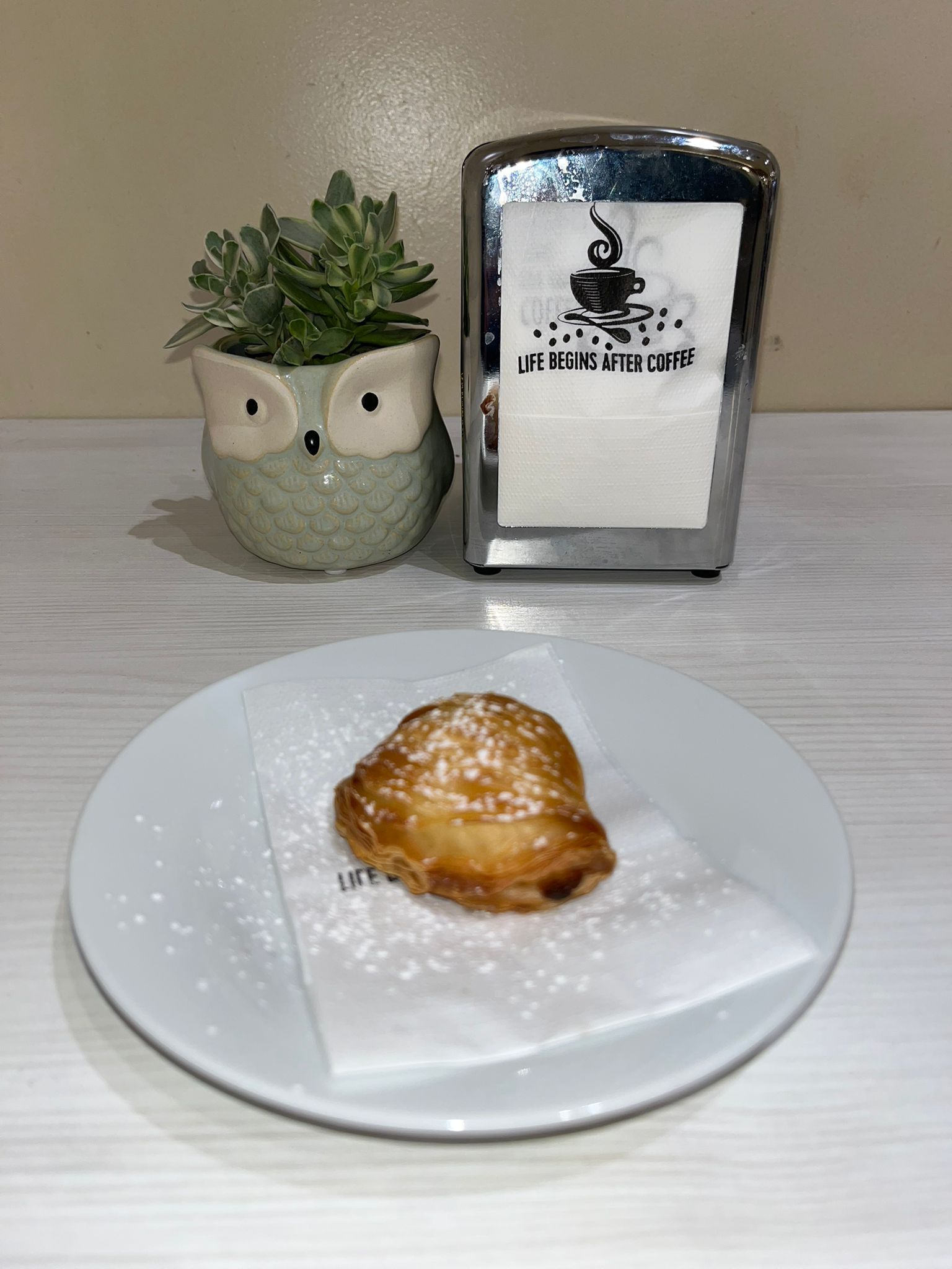 Pasta sfoglia su un piatto bianco spolverato di zucchero a velo, accanto a un vaso a forma di gufo e a un porta tovaglioli.