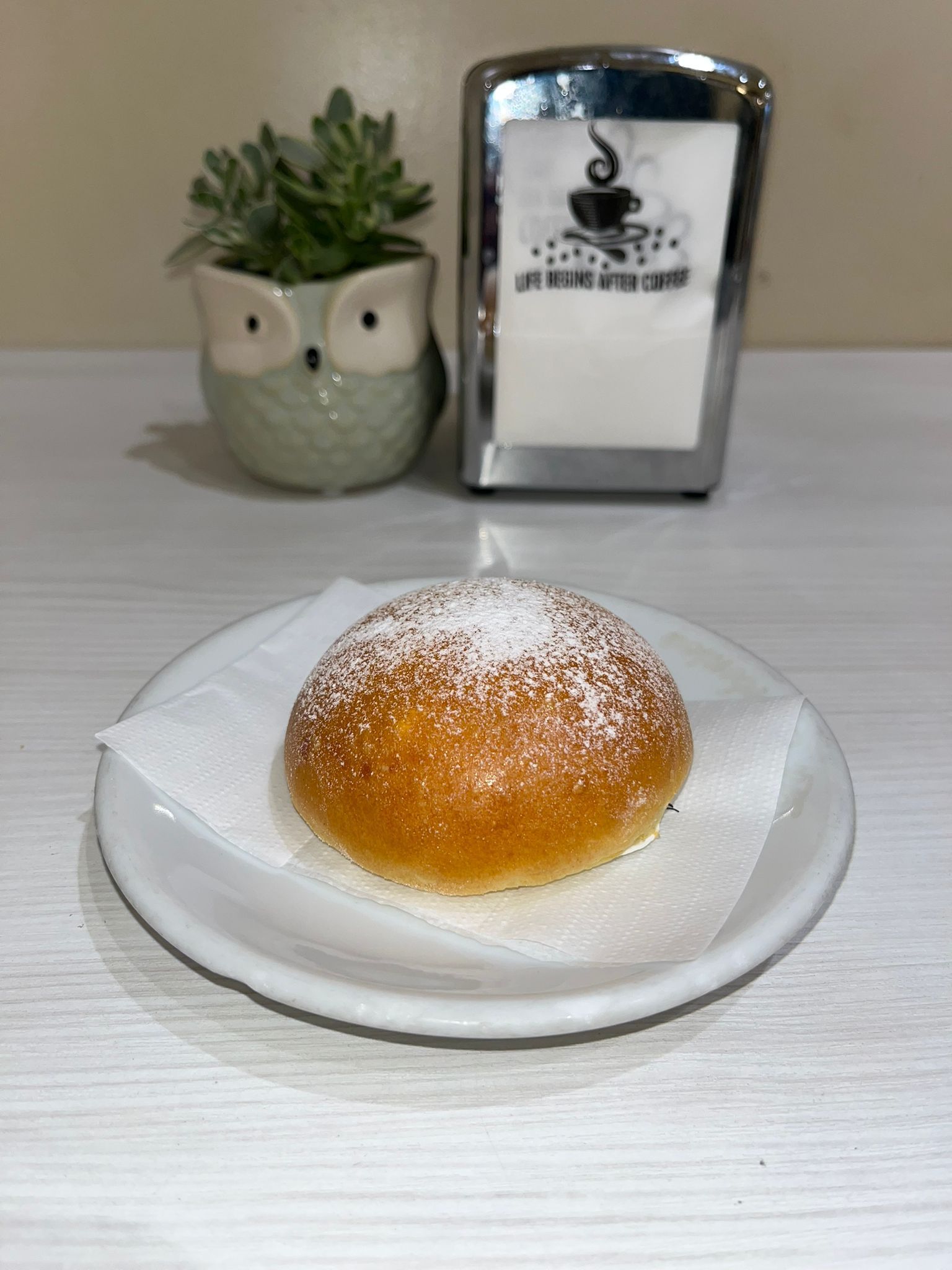 Pasta sfoglia su un piatto bianco con tovagliolo, spolverata di zucchero a velo, succulenta fioriera a forma di gufo, porta tovaglioli.