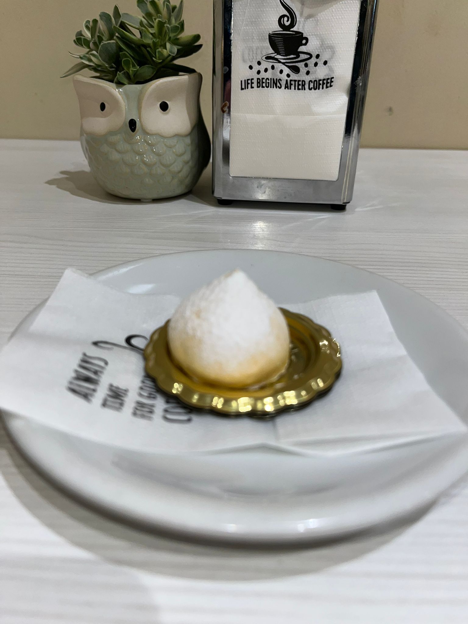 Dessert servito su un tappo di bottiglia dorato, con un tovagliolo su un piatto bianco.