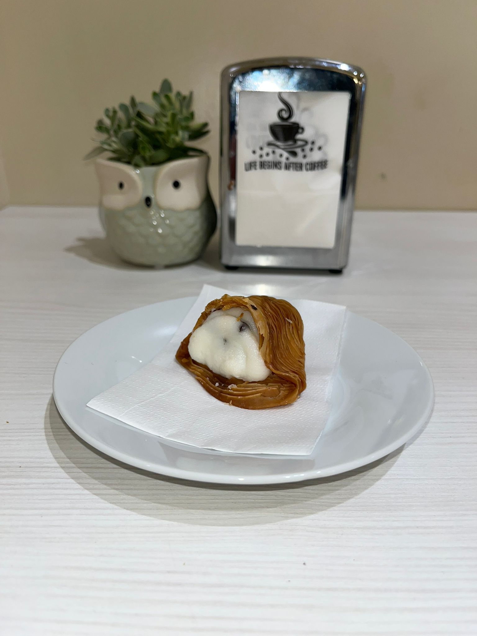 Pasta sfoglia su un piatto, con tovagliolo, fioriera a forma di gufo e porta tovaglioli su un bancone bianco.