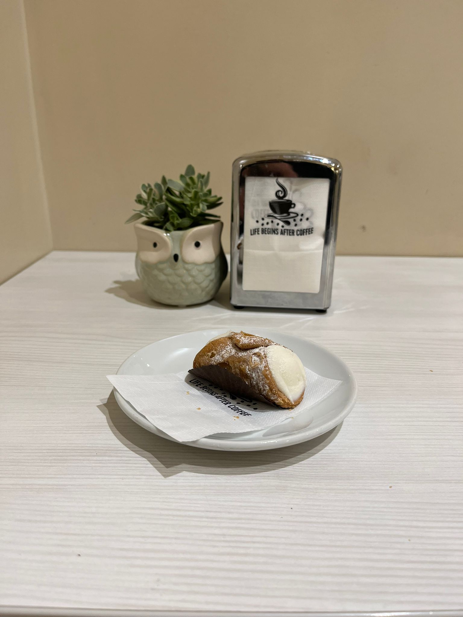 Cannoli su un piatto bianco con tovagliolo, accanto a un portavasi a forma di gufo e un porta tovaglioli su un tavolo bianco.