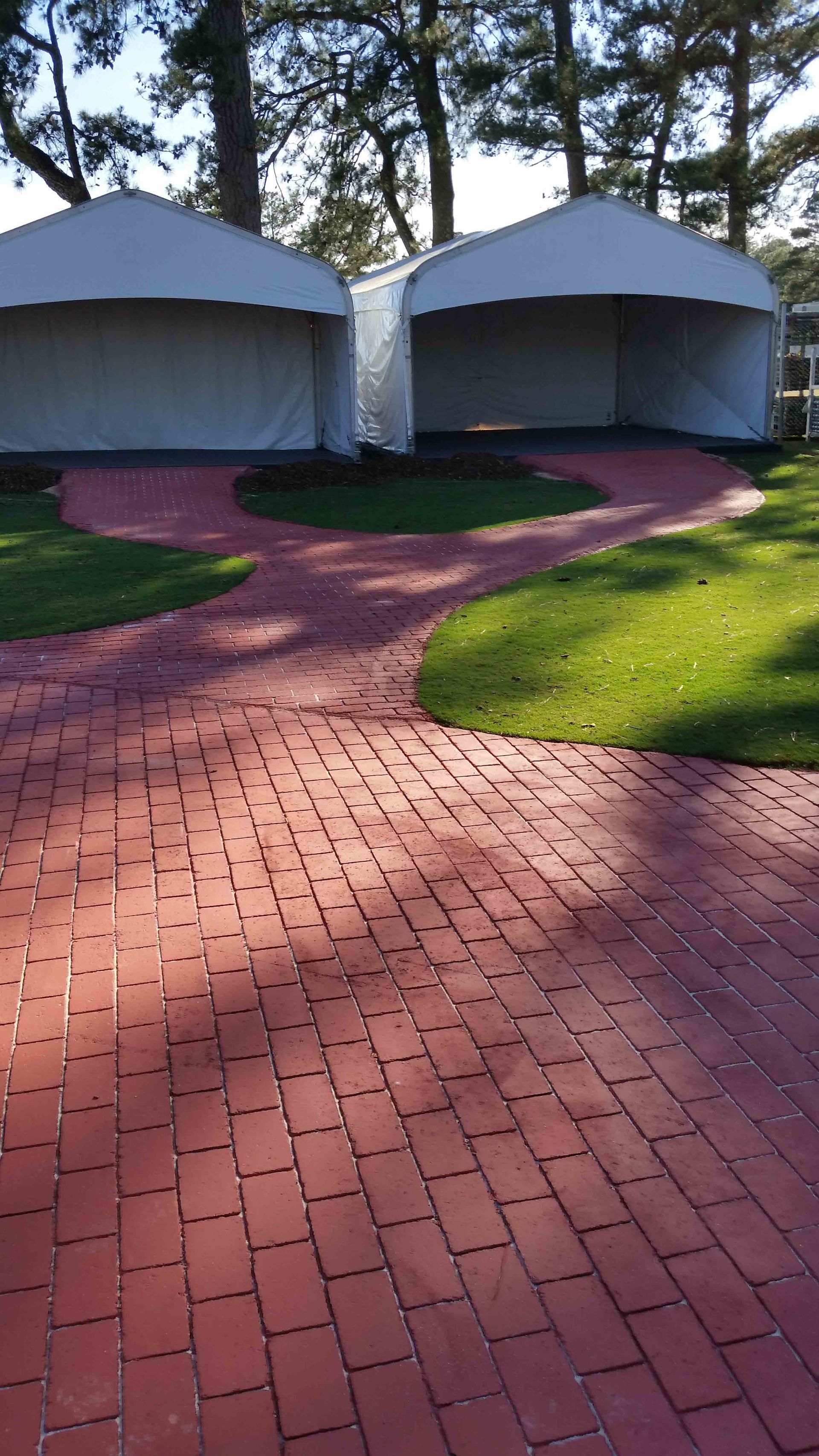 A red brick walkway leading to two white tents in a park.