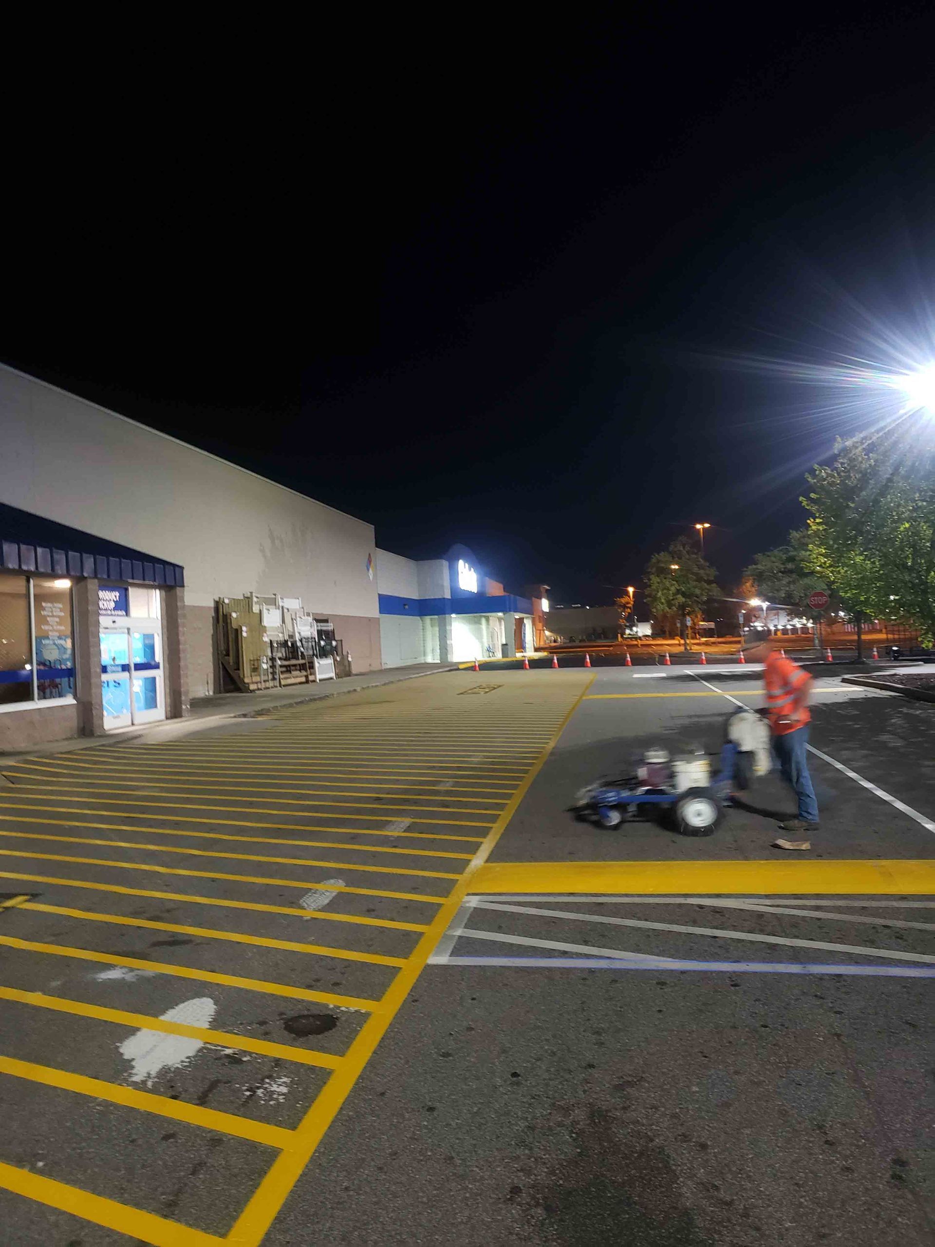 A man is painting yellow lines in a parking lot at night.
