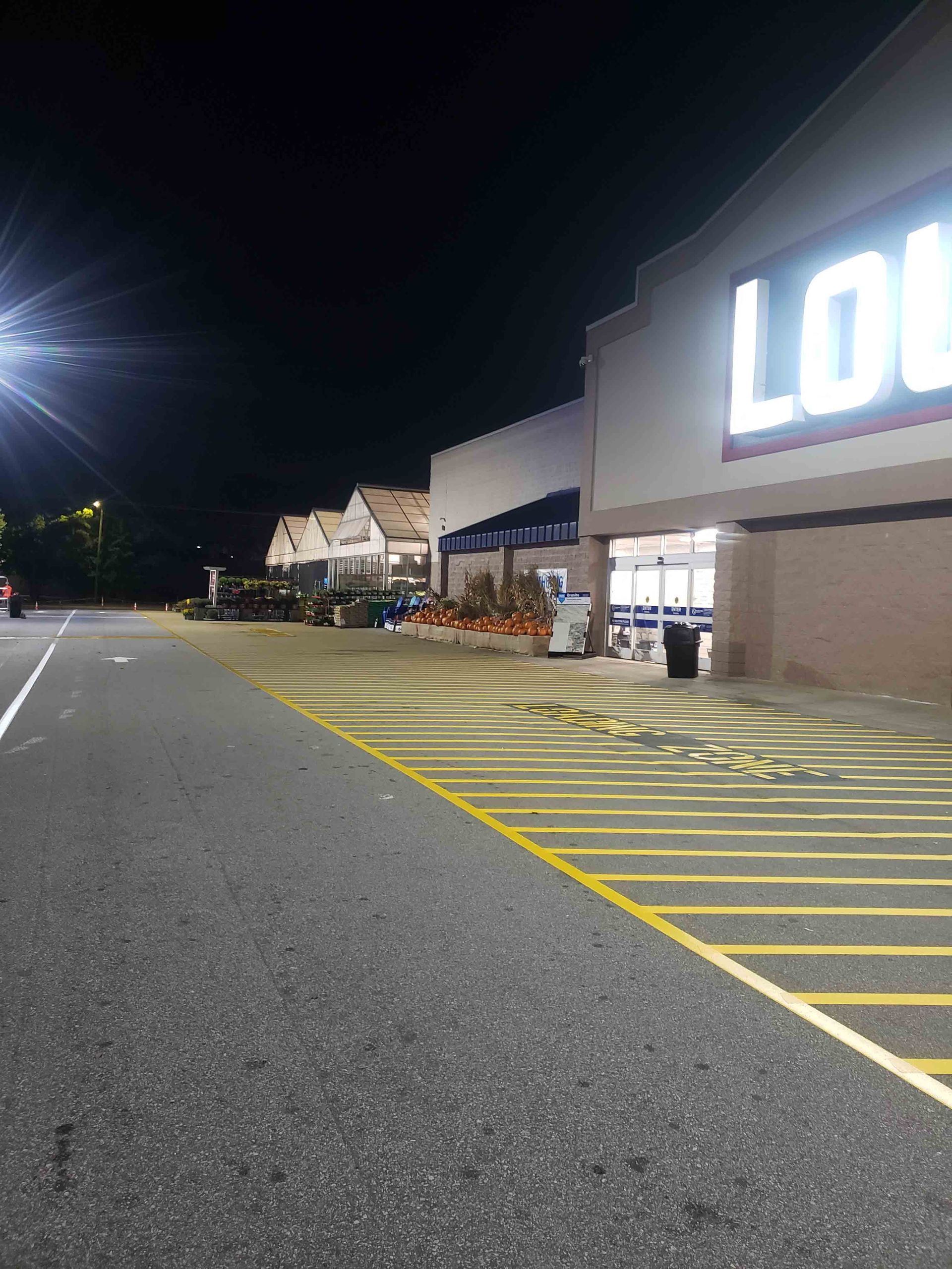 A large store is lit up at night with a parking lot in front of it.