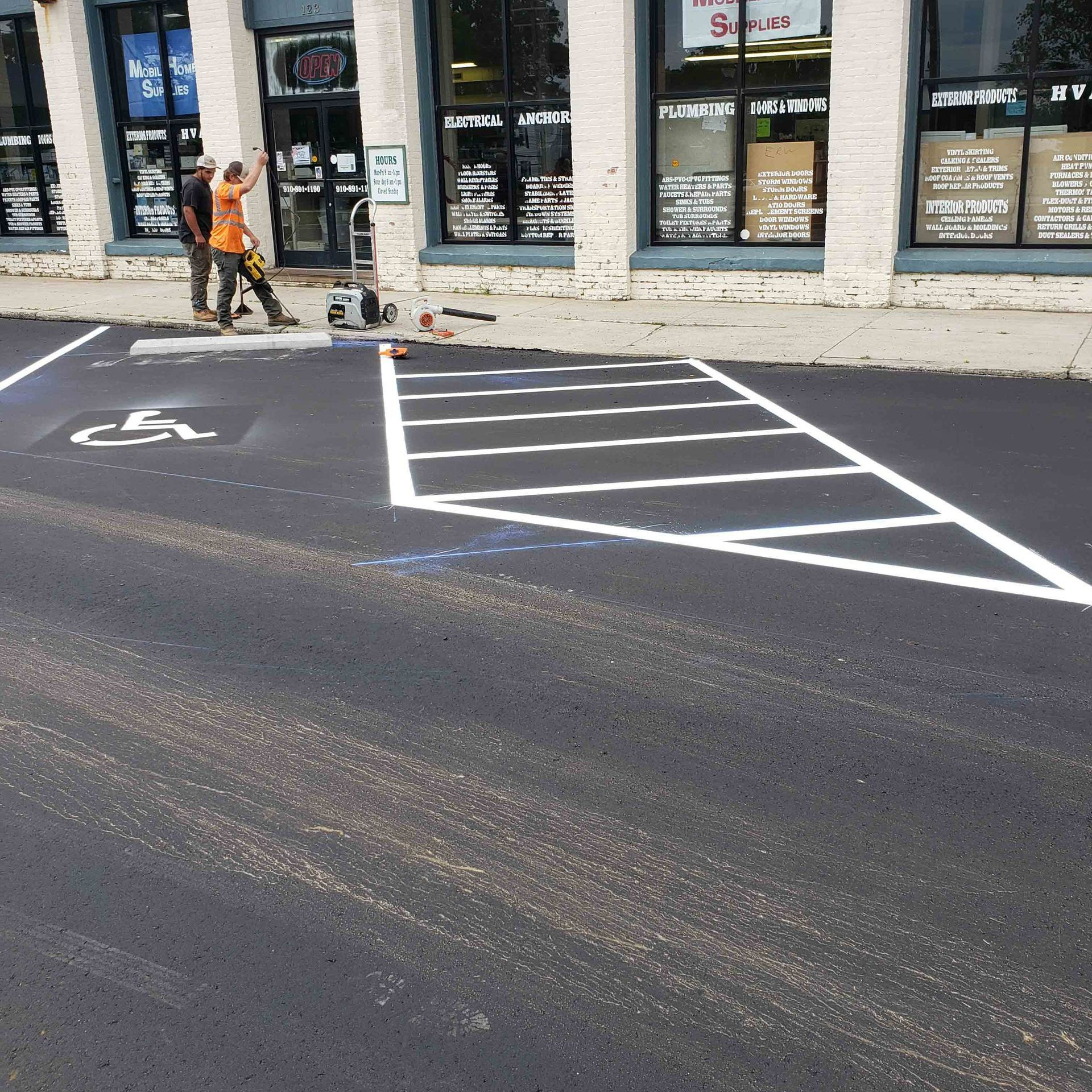 Two men are painting a handicapped parking space in front of a store