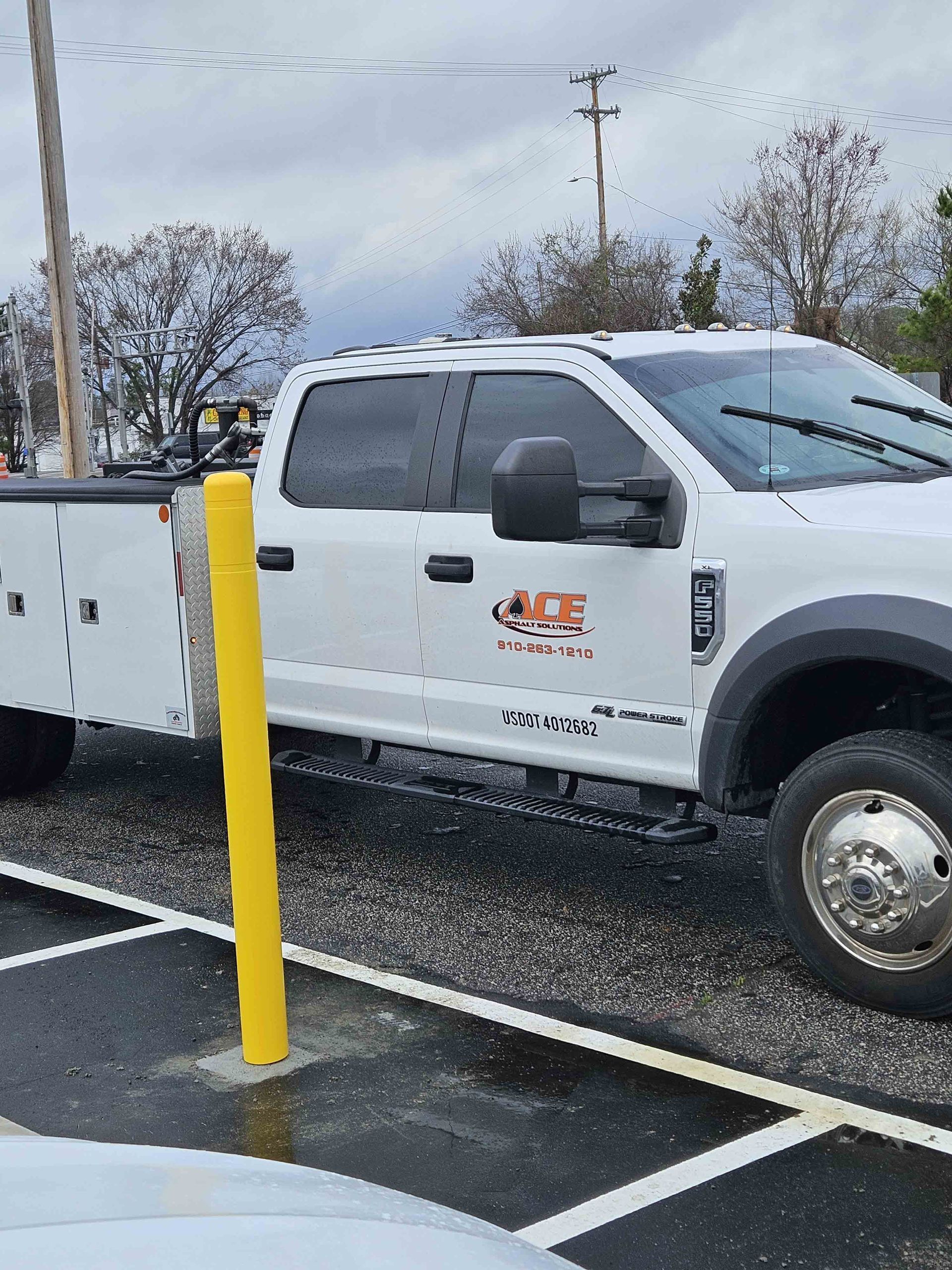 A white truck is parked in a parking lot next to a yellow pole.