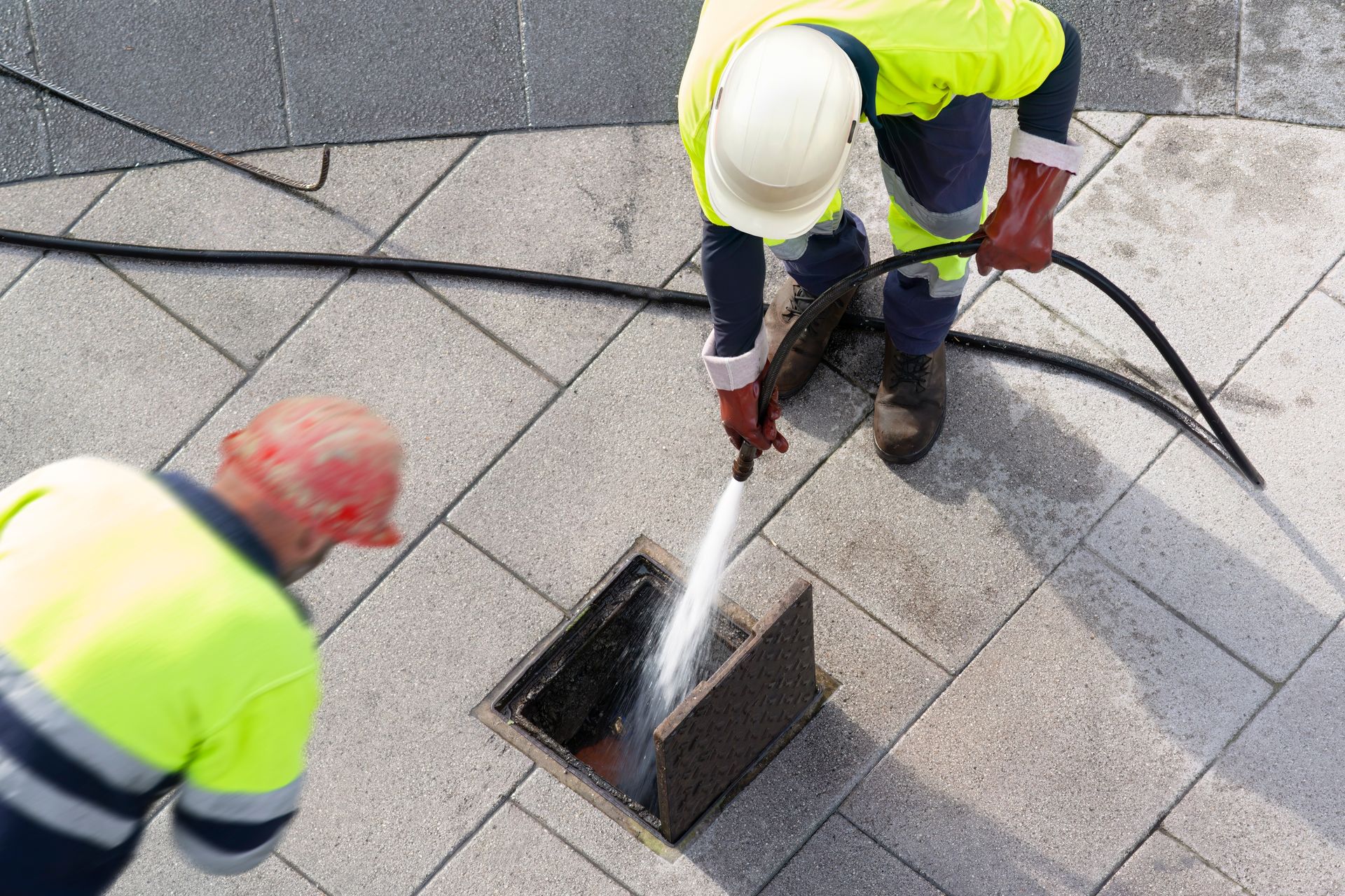 Two men are cleaning a manhole cover with a high pressure washer.