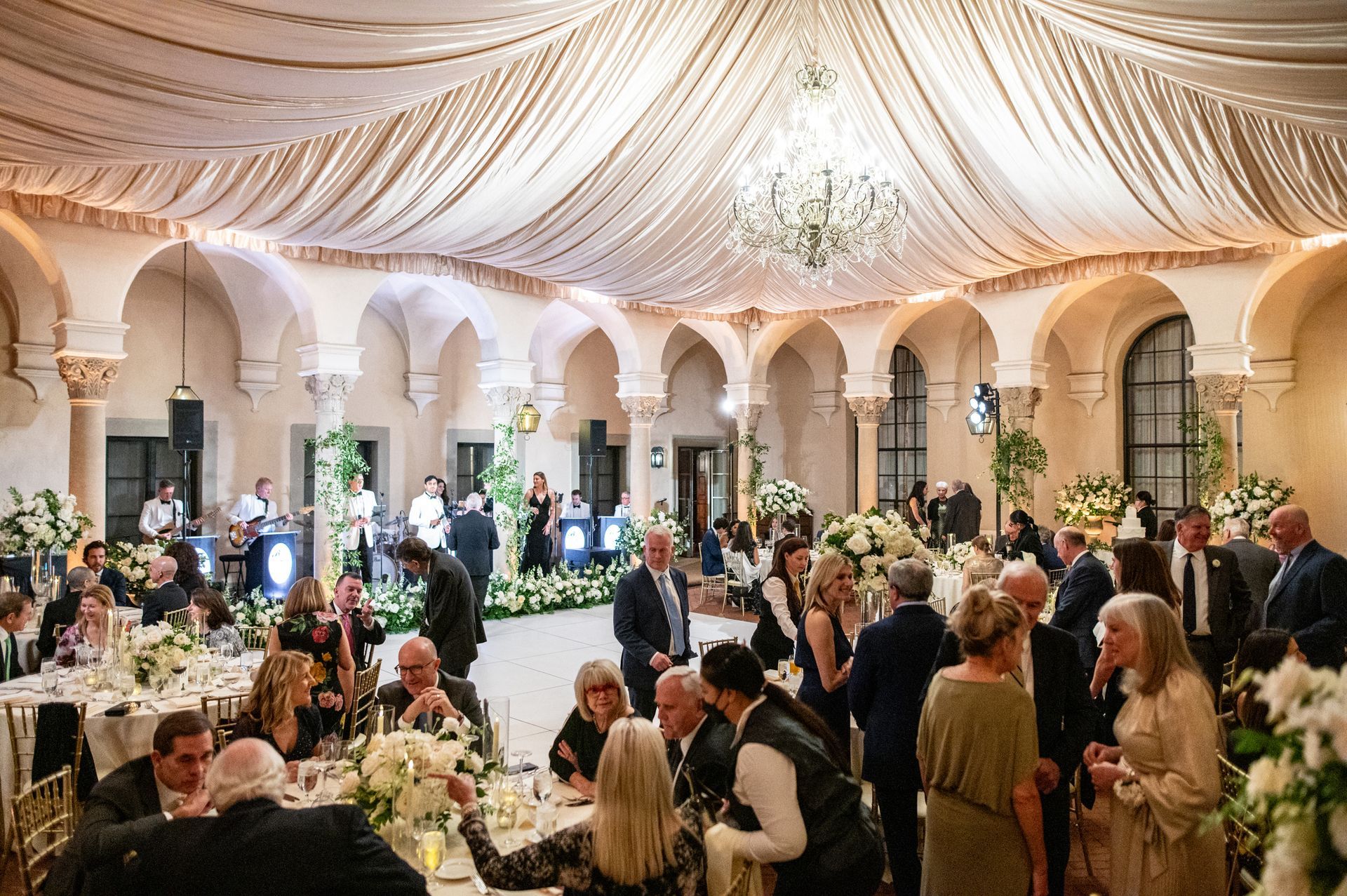 A group of people are sitting at tables in a large room at a luxury wedding reception.