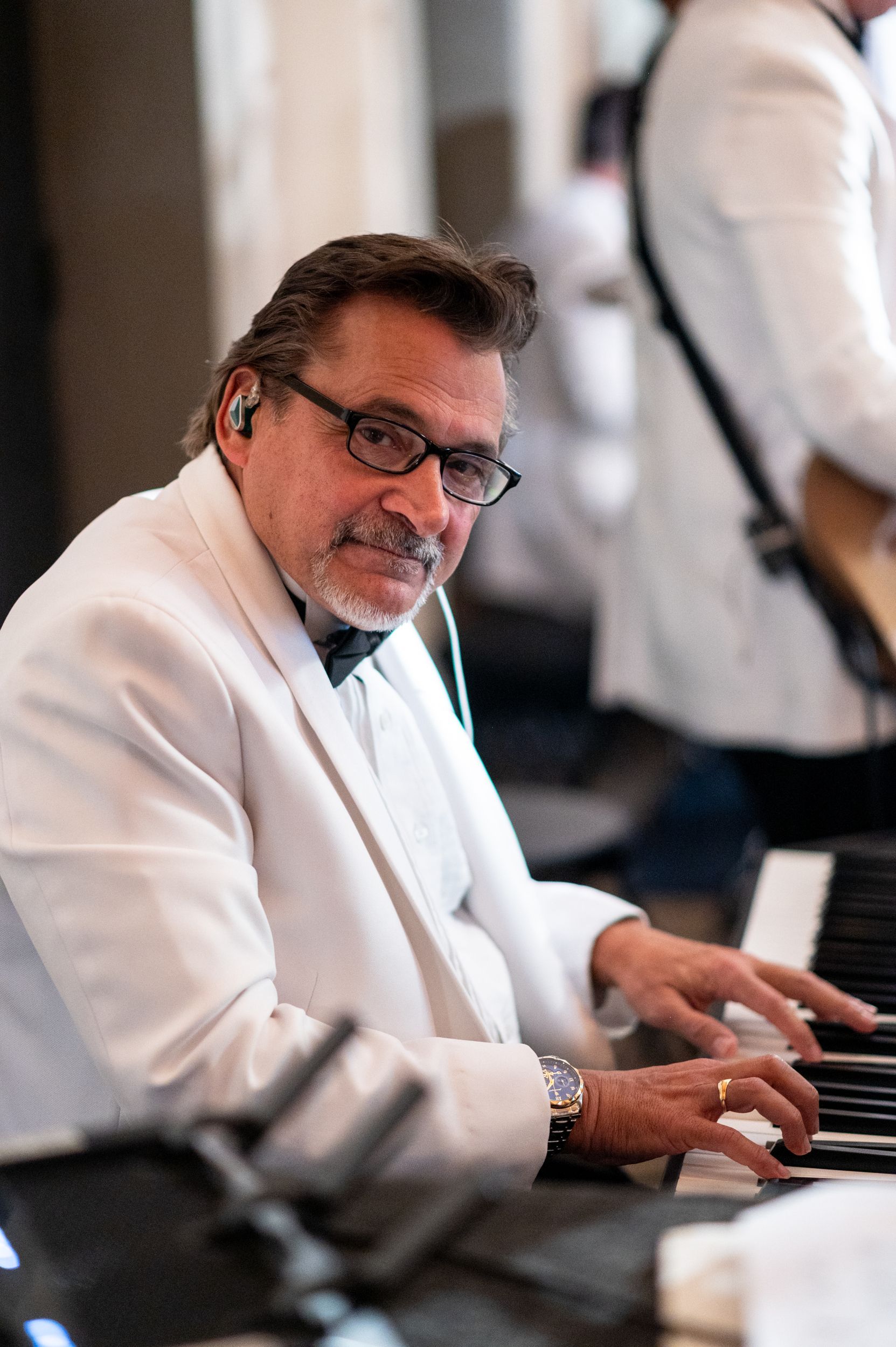 A man in a white suit is playing a piano.