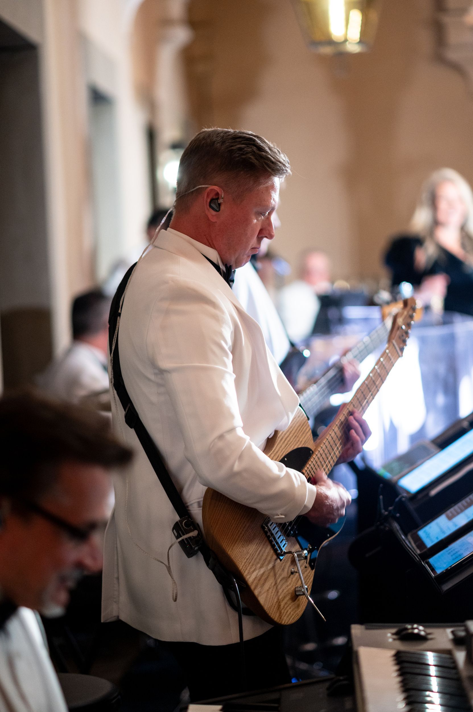 A man in a tuxedo is playing a guitar in a band.
