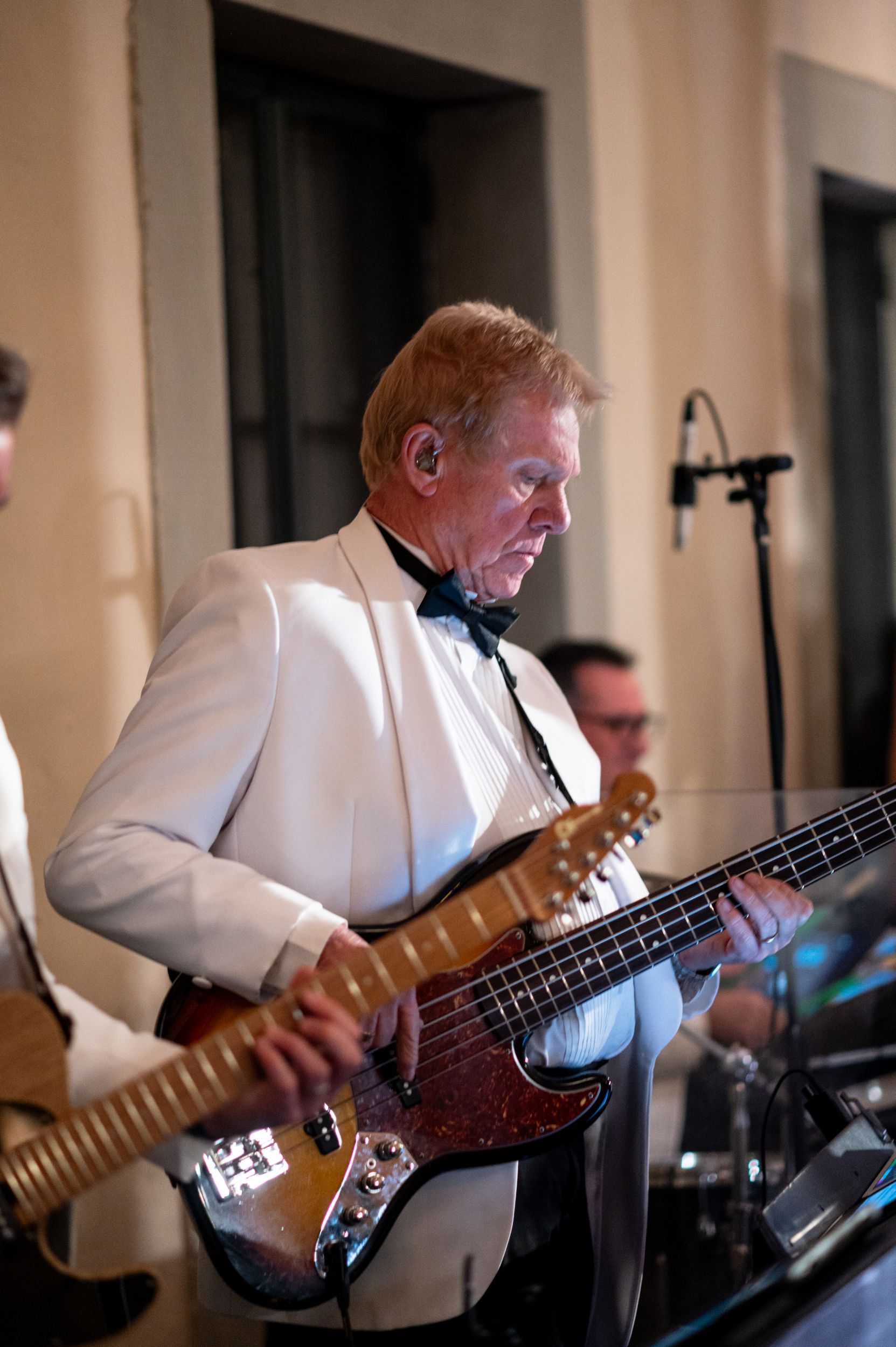 A man in a tuxedo is playing a guitar in a live band.