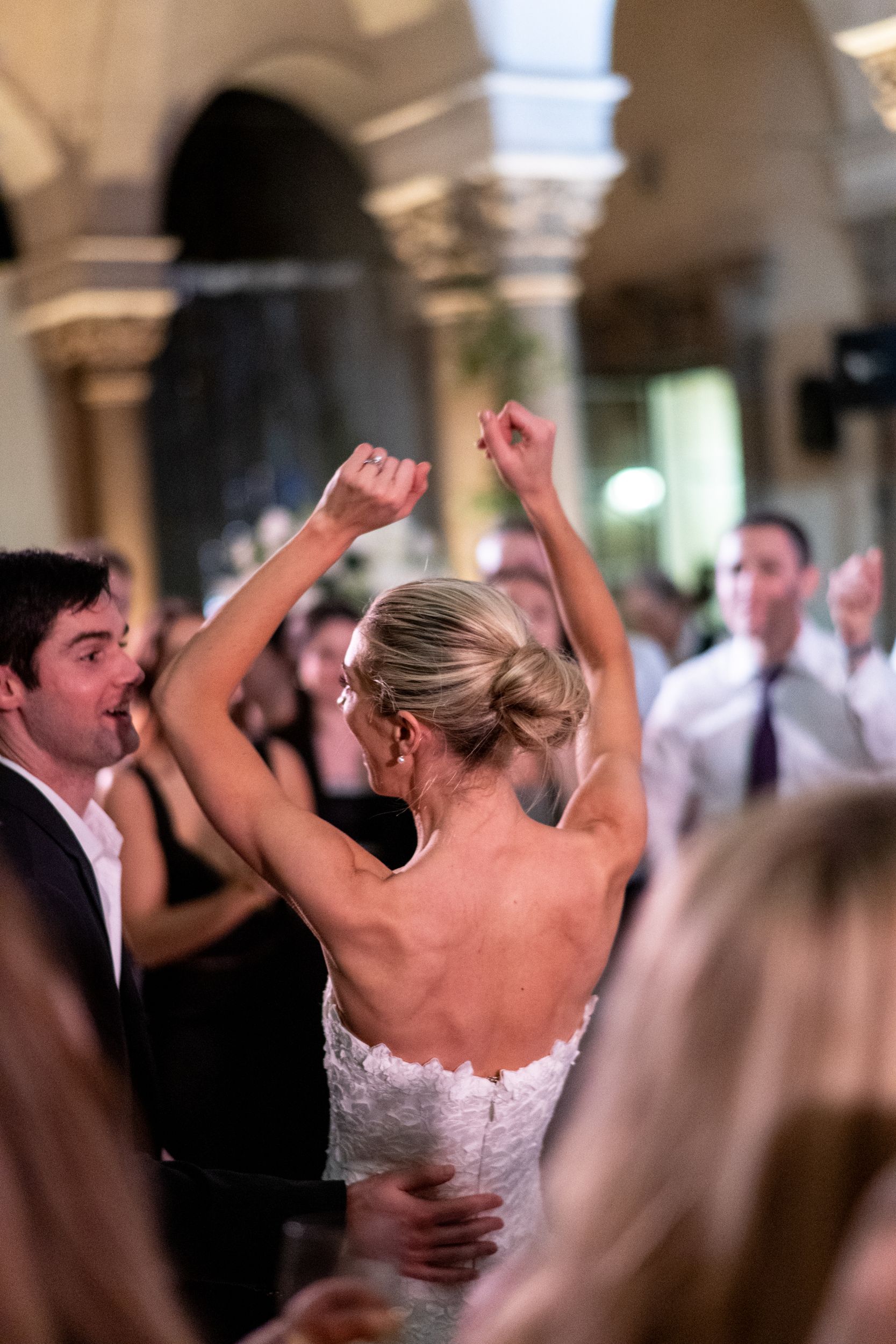 A bride and groom are dancing at their wedding reception with their arms in the air.