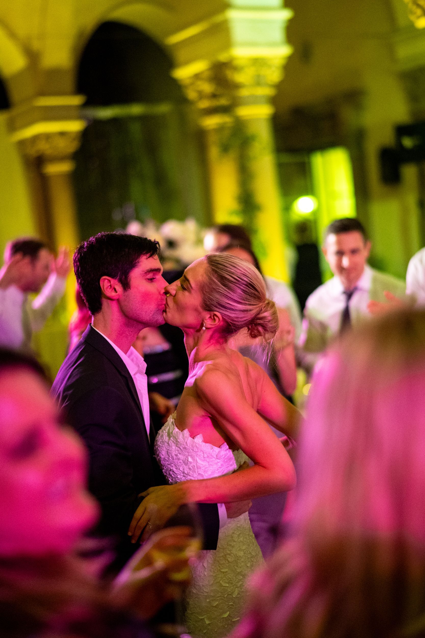 A bride and groom are kissing on the dance floor at their wedding reception.