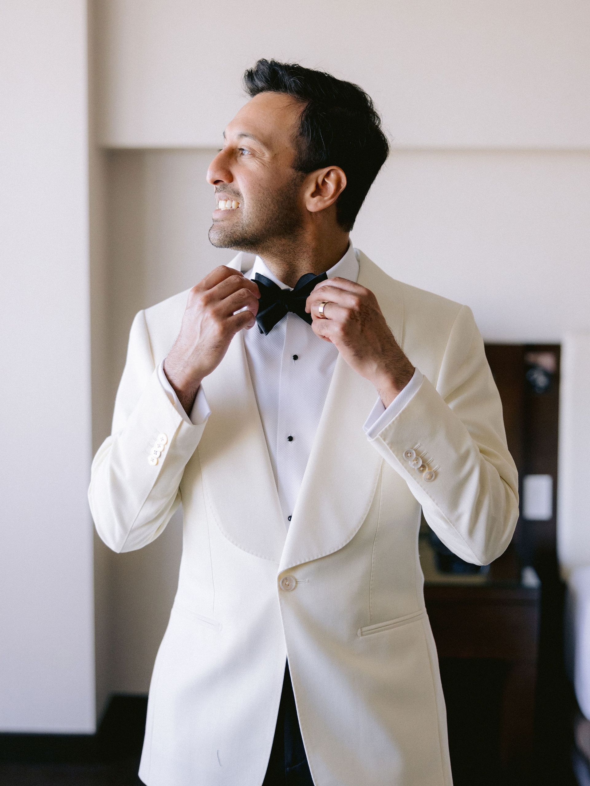 The man is wearing a white tuxedo and a black bow tie.