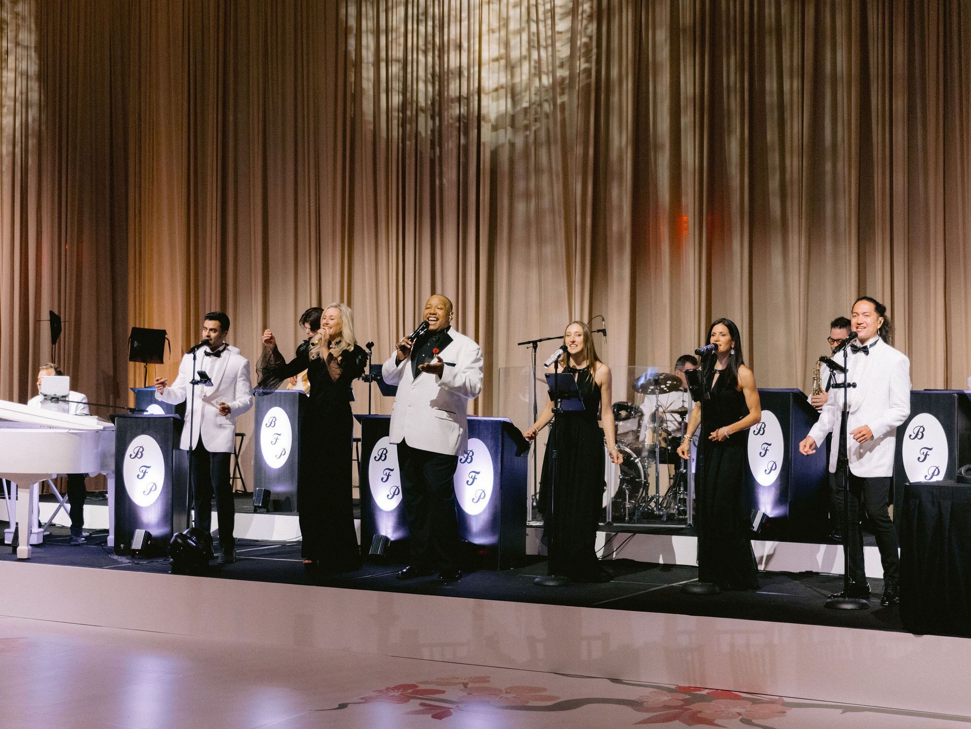 A group of people are standing on a stage singing into microphones.