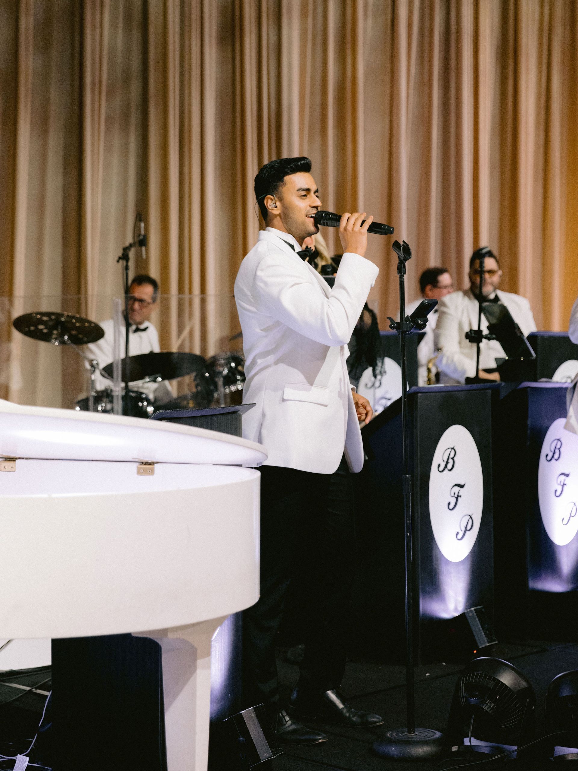 A man in a tuxedo is singing into a microphone in front of a band.