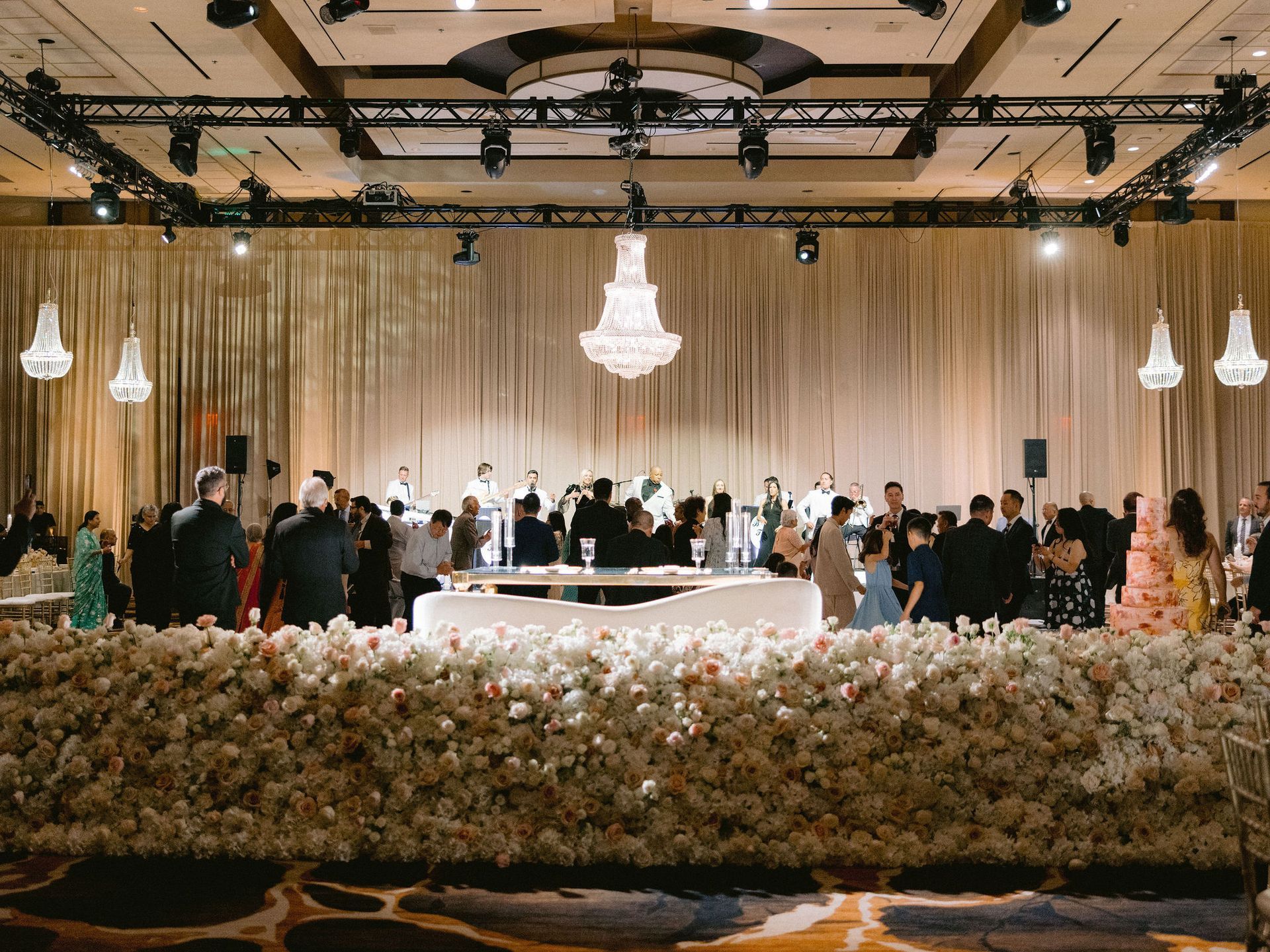 A group of people are standing around a table in a large room at a wedding reception.