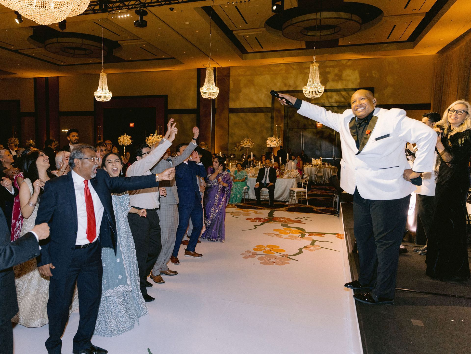 A man in a white suit is standing in front of a crowd of people