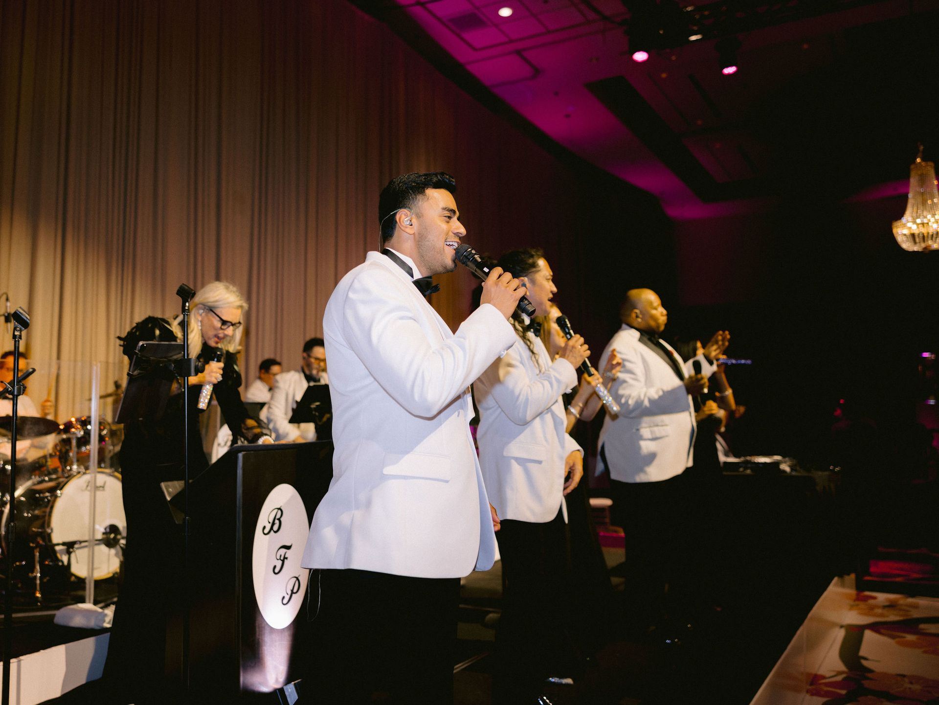 A group of men in tuxedos are singing into microphones on a stage.