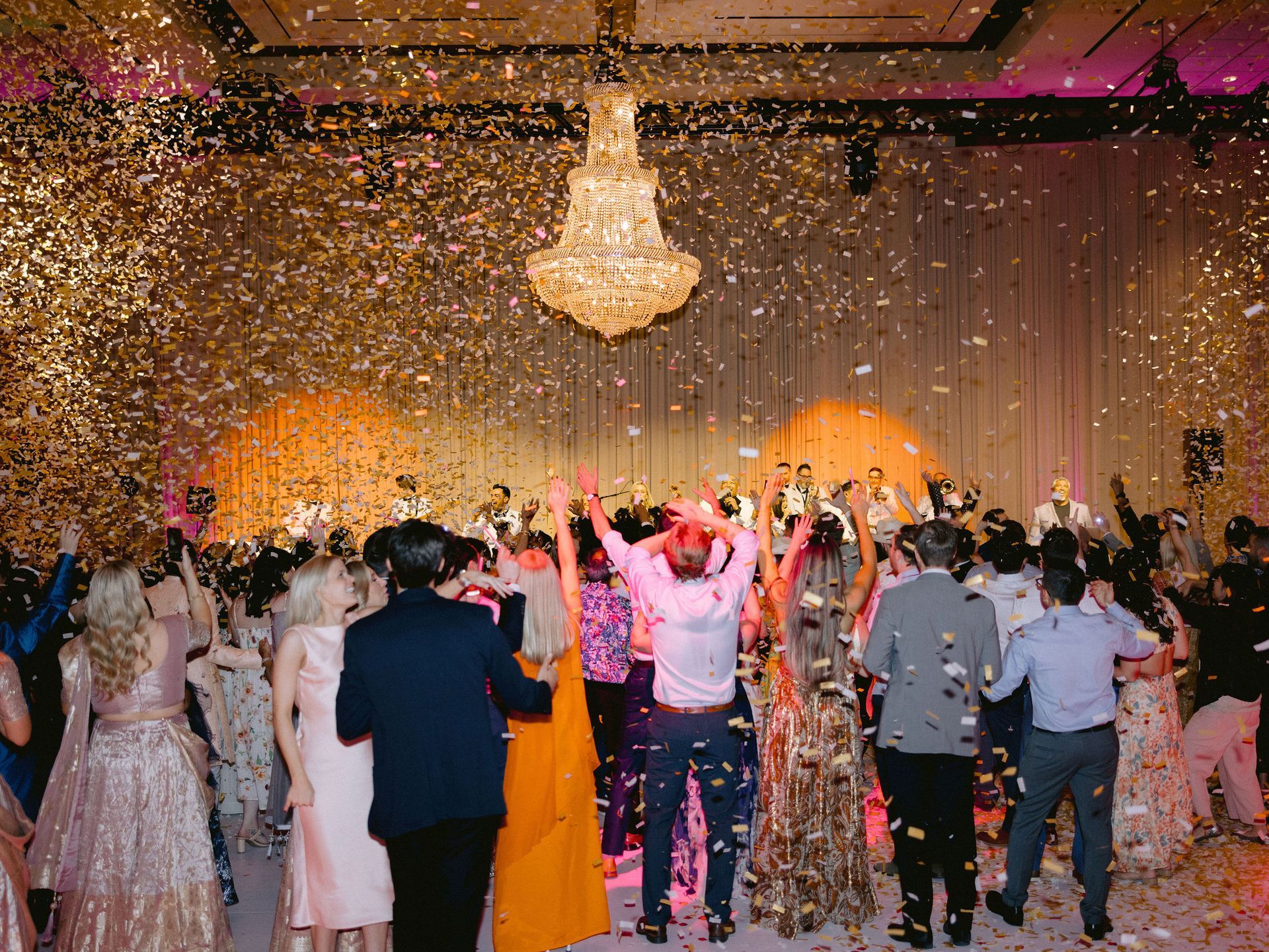 A group of people are dancing in a room with confetti falling from the ceiling.