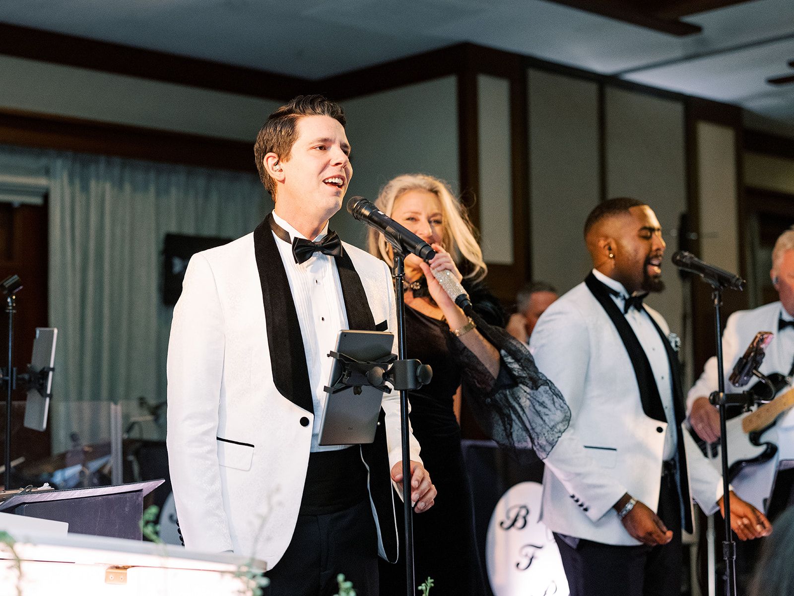Live band singing on stage in white tuxedos