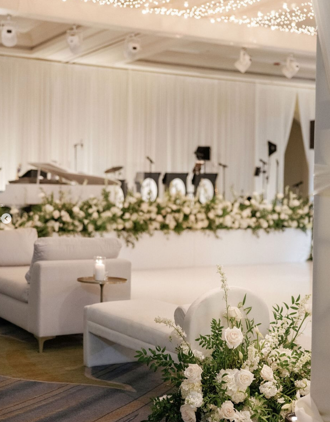 Elegant all-white wedding reception. Stage backdrop, floral arrangements, and seating create a sophisticated atmosphere.