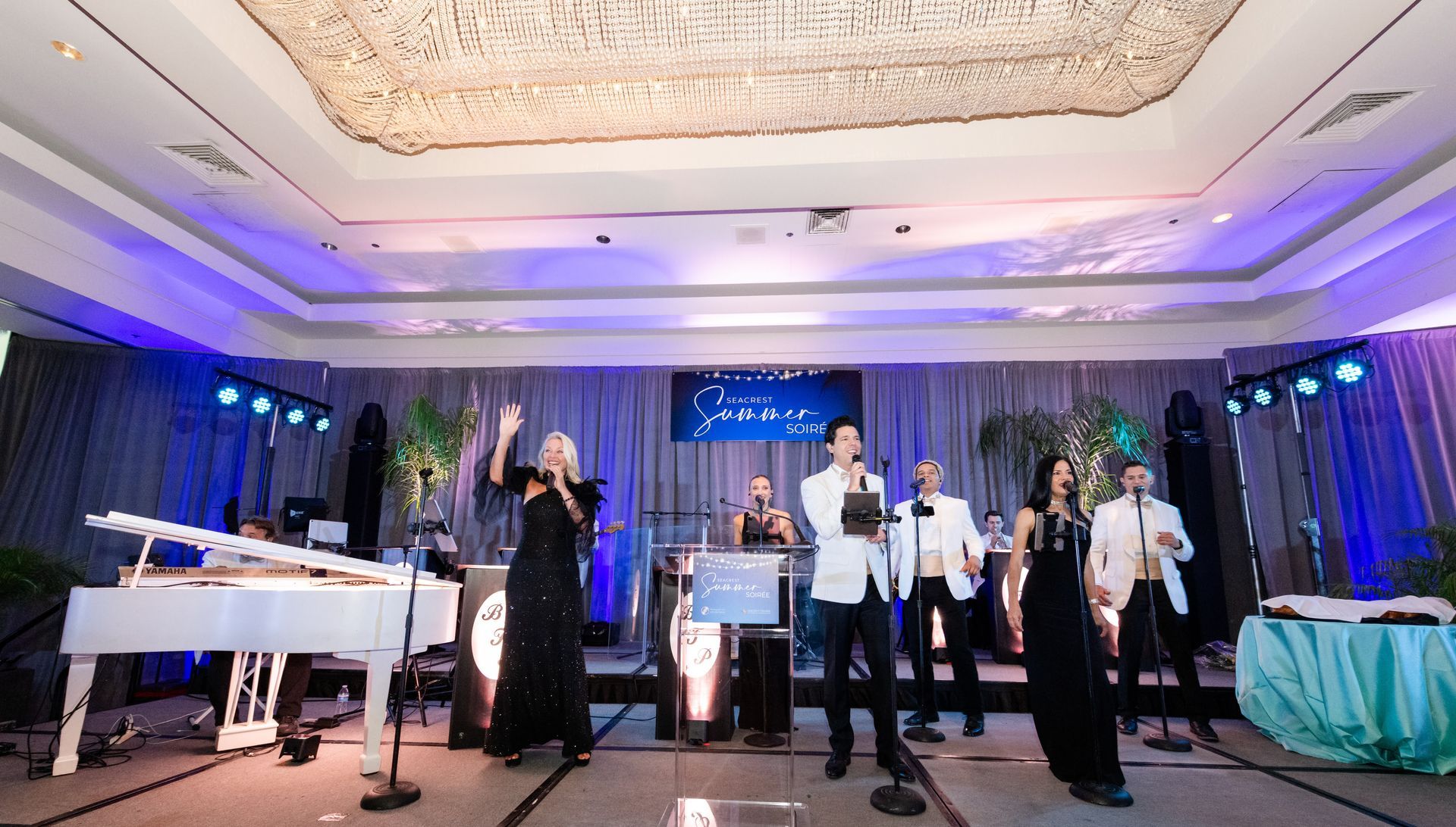 A band performing on a stage. People in formal attire, stage lit with blue and white lights.