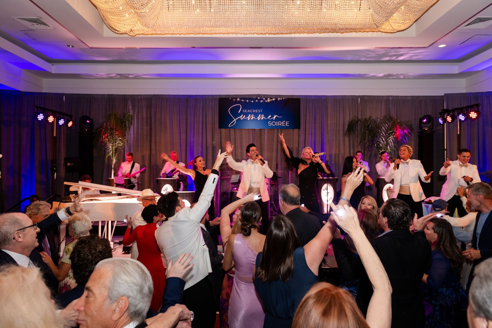 A band performing on stage at an event, with dancers in the foreground; colorful lights.