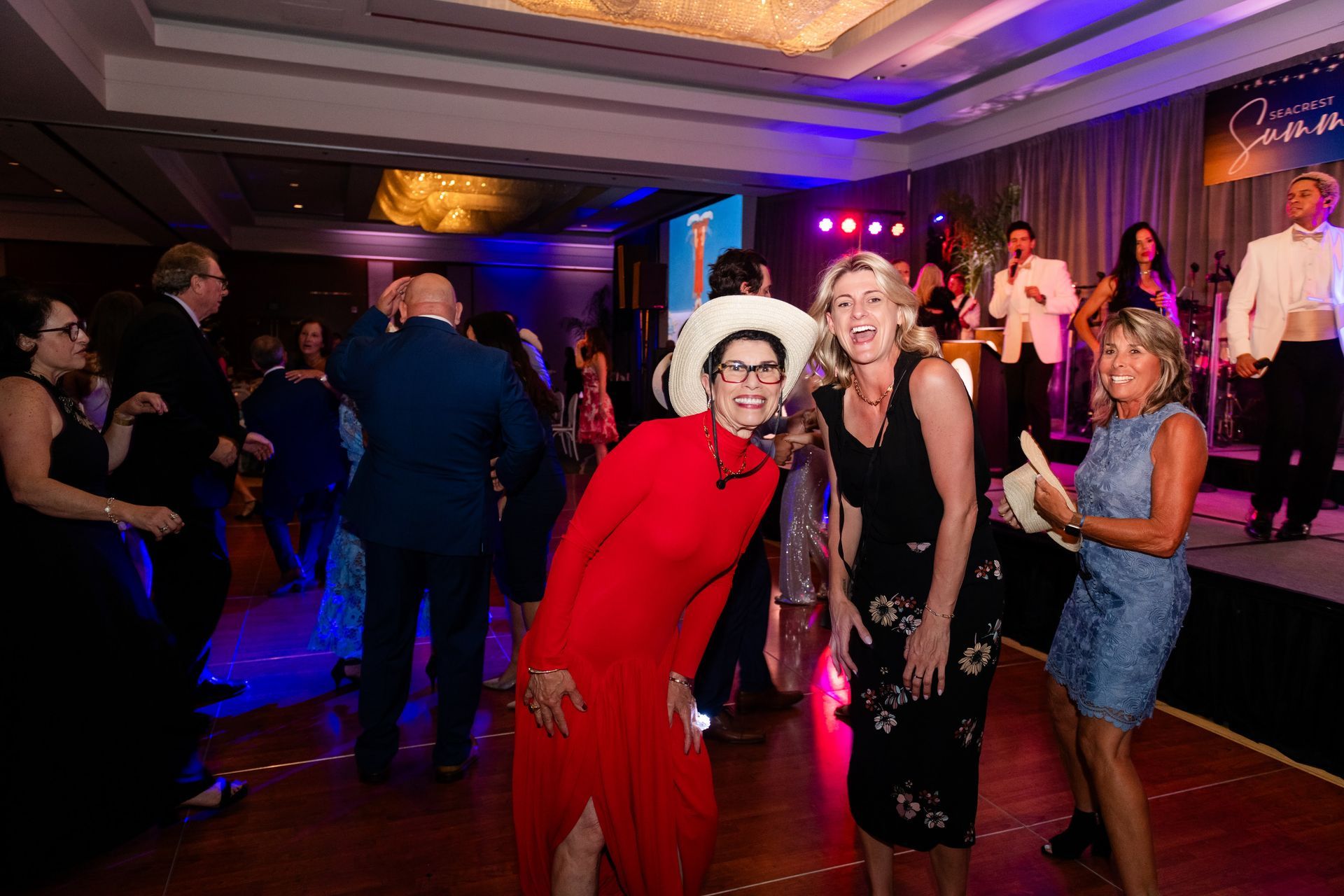 People dancing at a formal event with a band on stage. Red, black, and blue dresses.