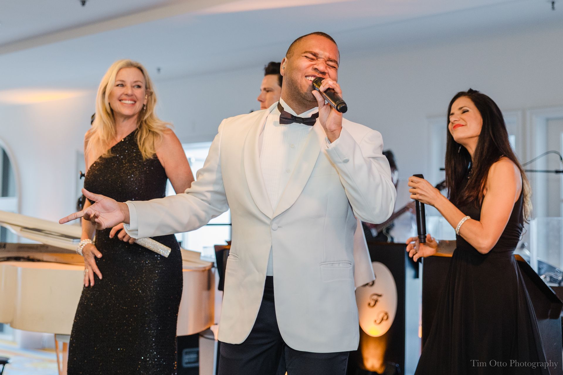 A band performing at wedding: a singer in a white suit, two female vocalists in black dresses, and a piano.