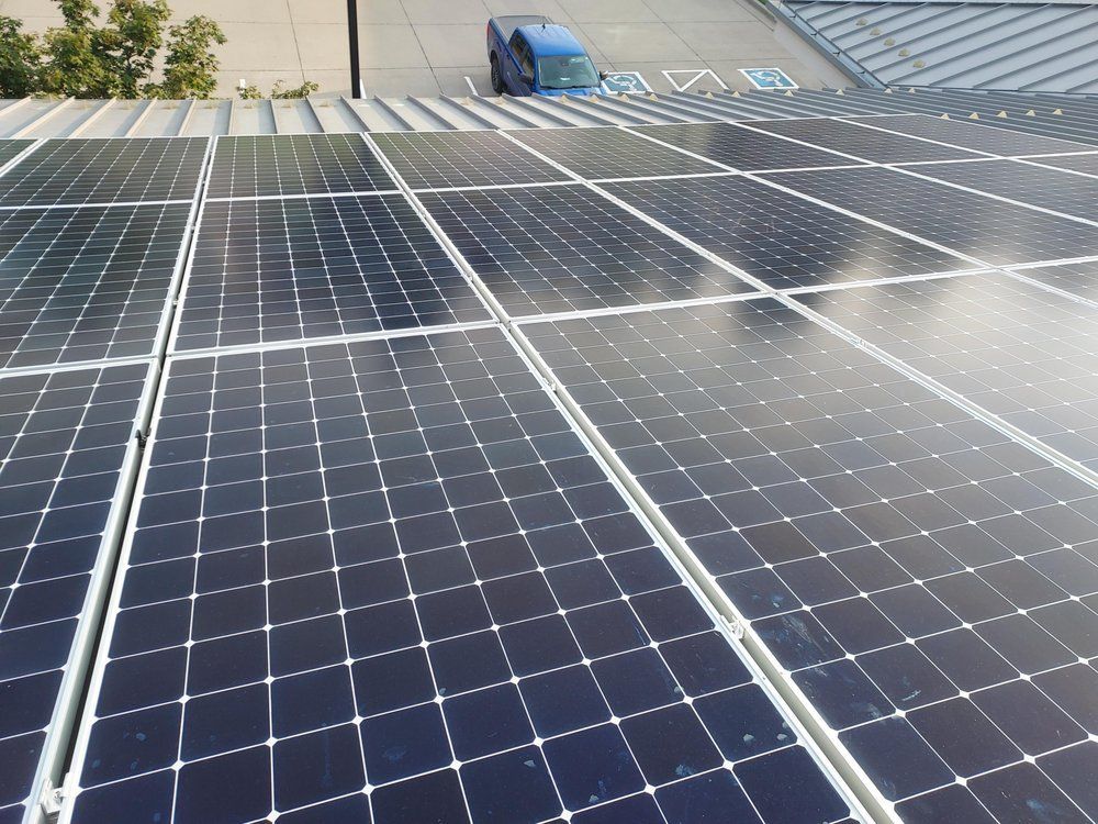 Solar panels on a roof, reflecting sunlight. A blue vehicle and a building are visible in the background.
