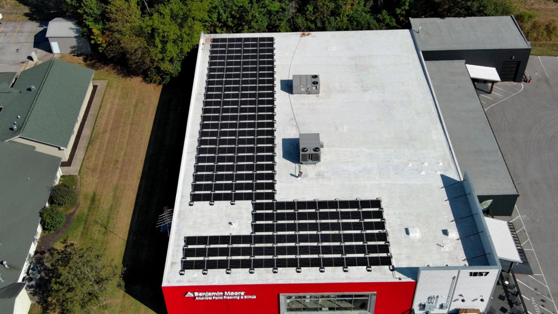 Aerial view of a flat commercial building roof with partial solar panel installation over a red facade.