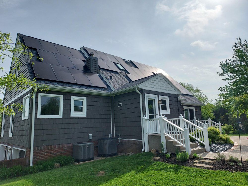 House with dark roof solar panels, gray siding, white trim, and a sunny sky.