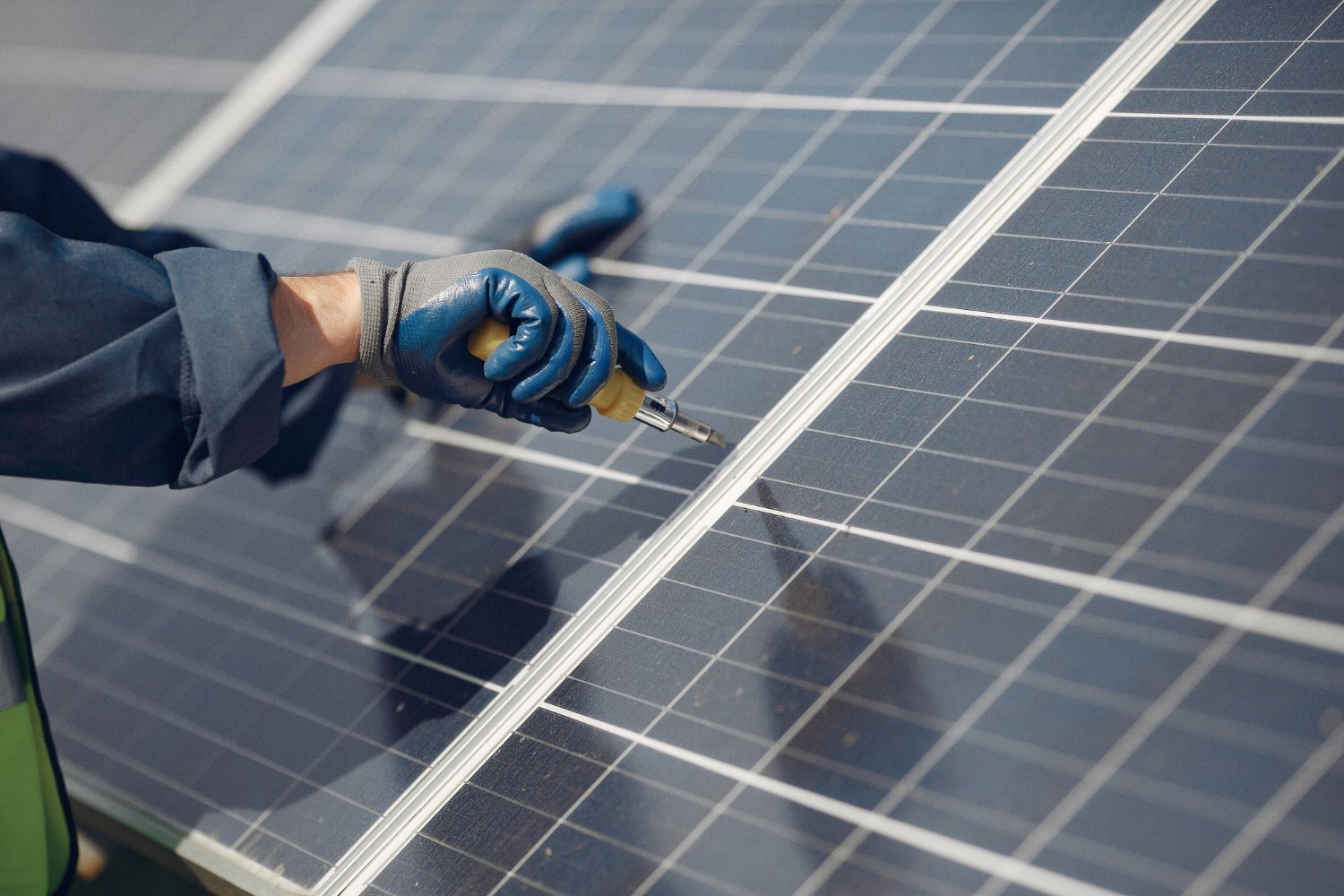 A close-up view of a gloved hand using a screwdriver to tighten a metal fastener on a solar panel array.