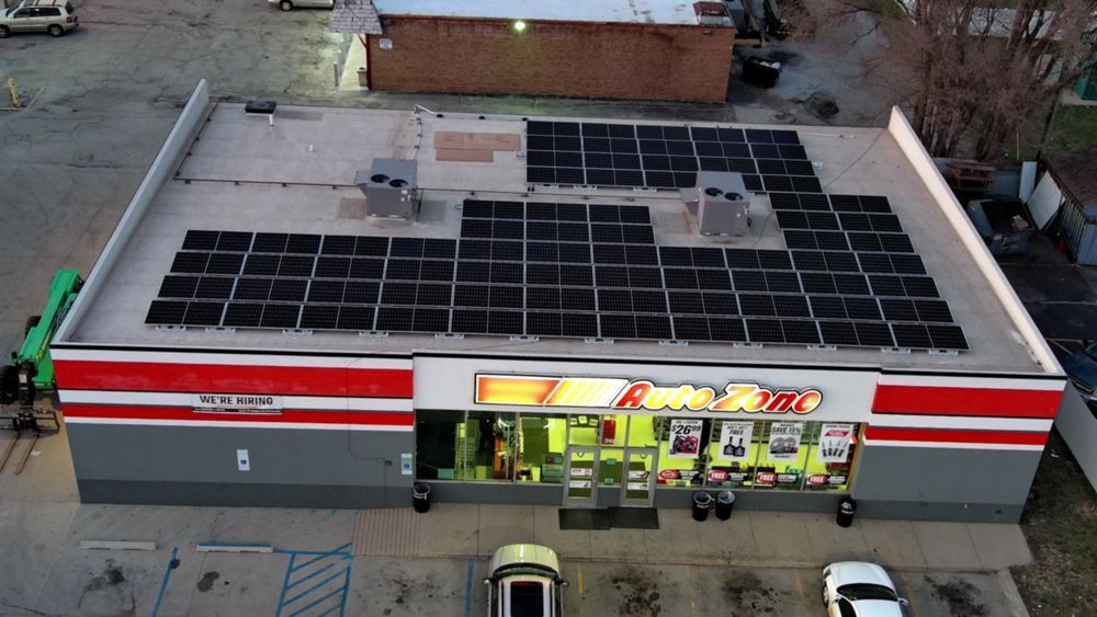 A convenience store with solar panels on the roof. Red and white striped trim, storefront entrance.