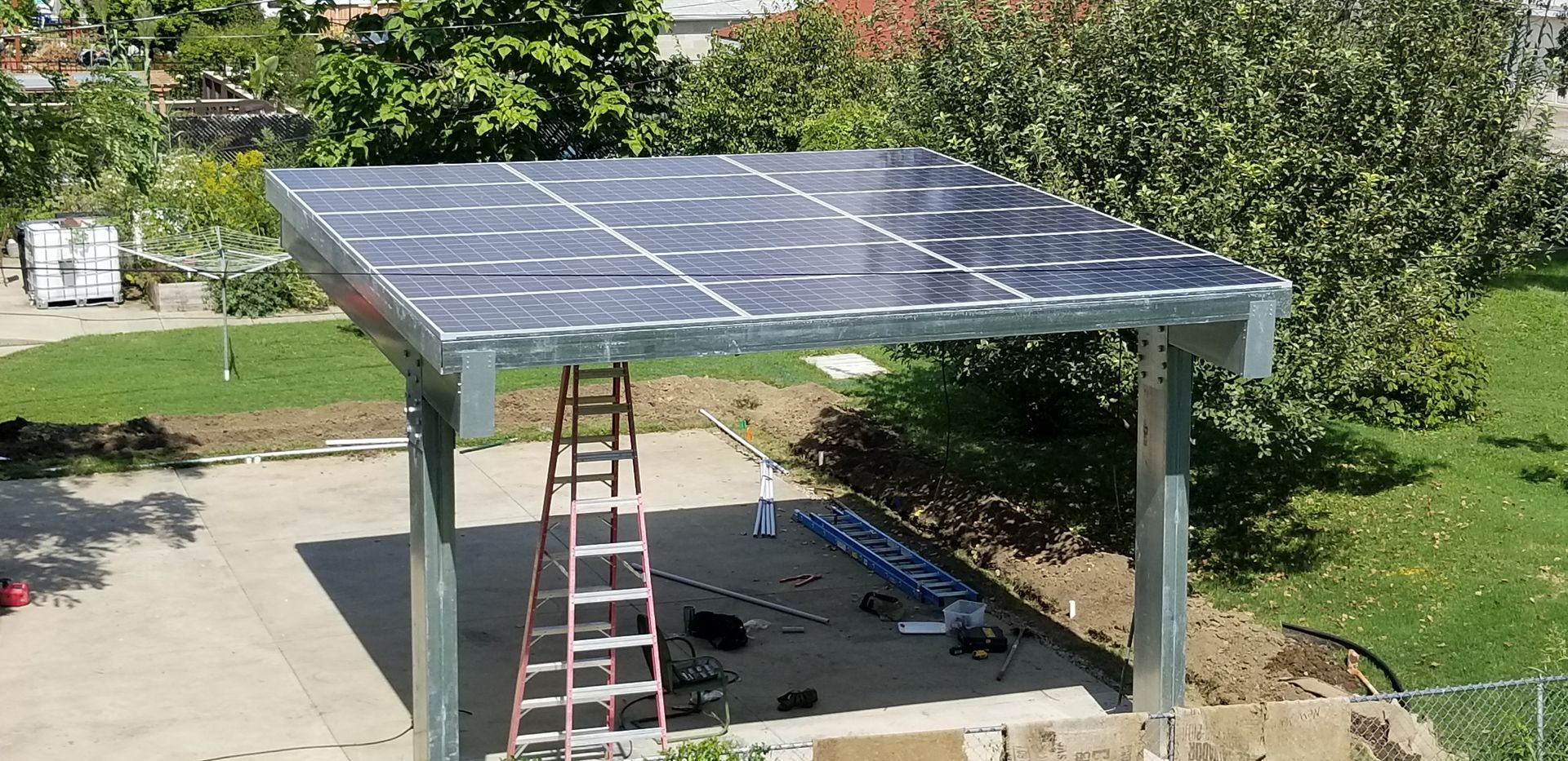 Solar panel canopy with a ladder in a yard.