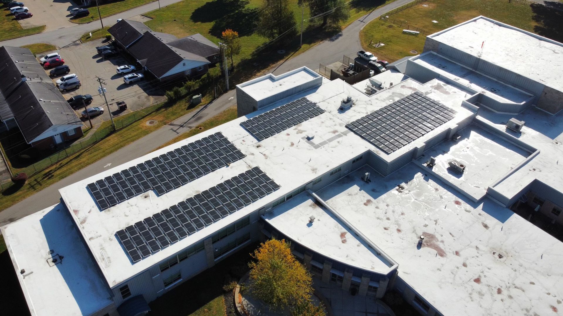 Aerial view of a building roof covered with solar panels. A parking lot is visible next to it.