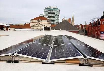 Solar panels on a flat roof with buildings and a cityscape in the background.