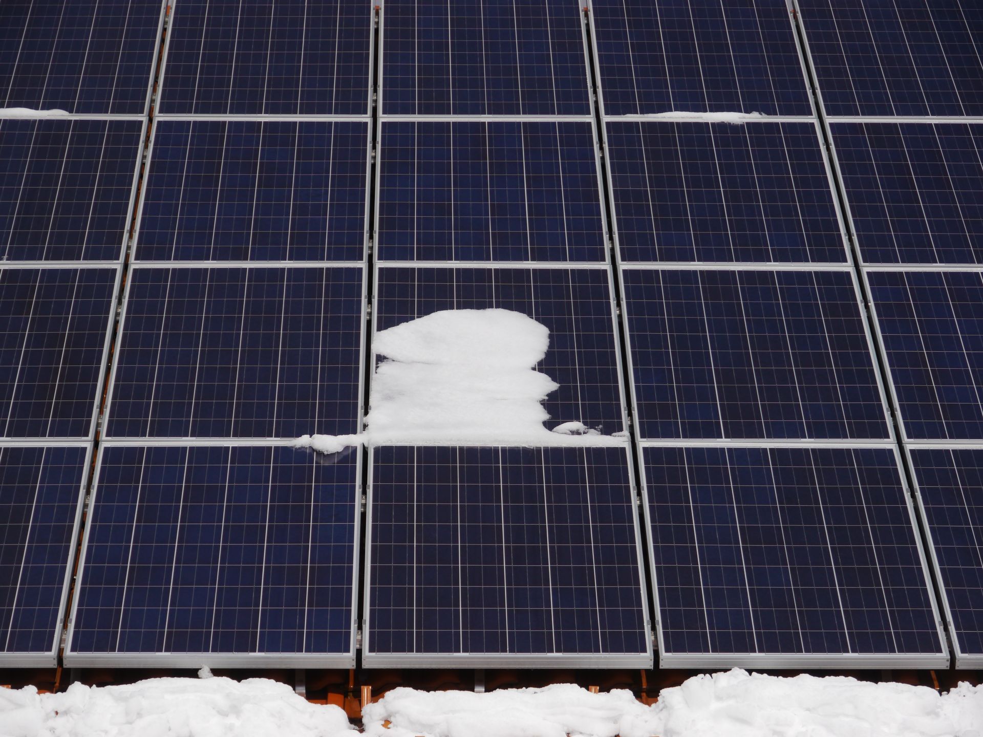 Solar panels covered in snow, with a significant amount of snow accumulating on one panel.