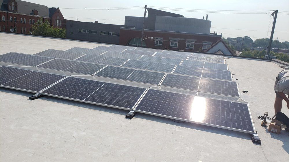 Solar panels installed on a flat rooftop in front of a brick building. A person is on the right.