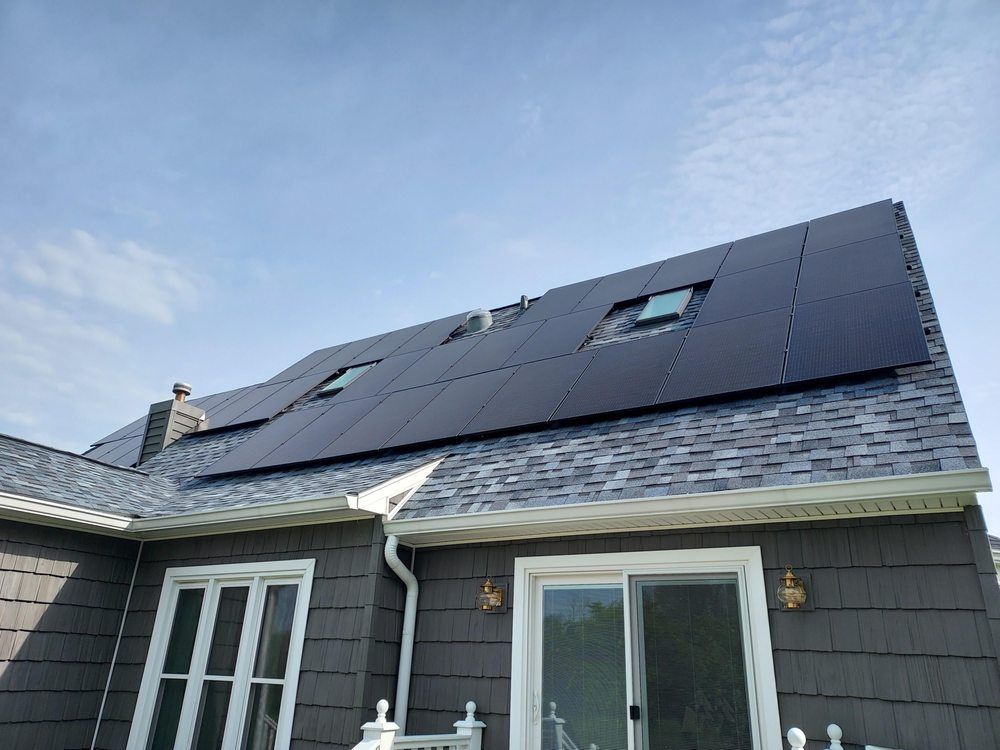 Solar panels on a gray shingled roof of a house with gray siding and a clear blue sky.