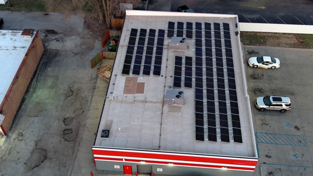 Solar panels on the roof of a commercial building with red and white trim, two cars in parking lot.