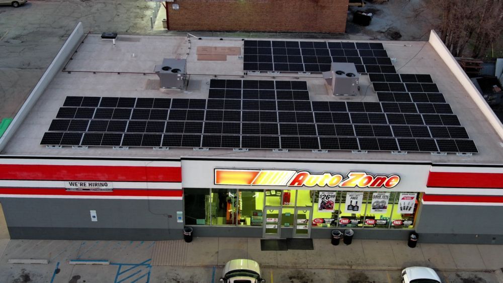 AutoZone store with solar panels on the roof, lit entrance, cars parked in front.