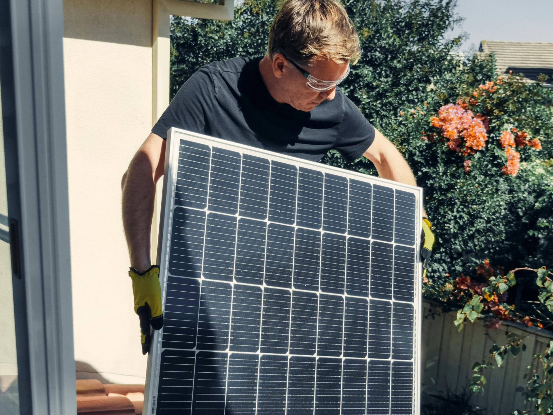 Man in glasses, holding solar panel on rooftop, installing renewable energy.