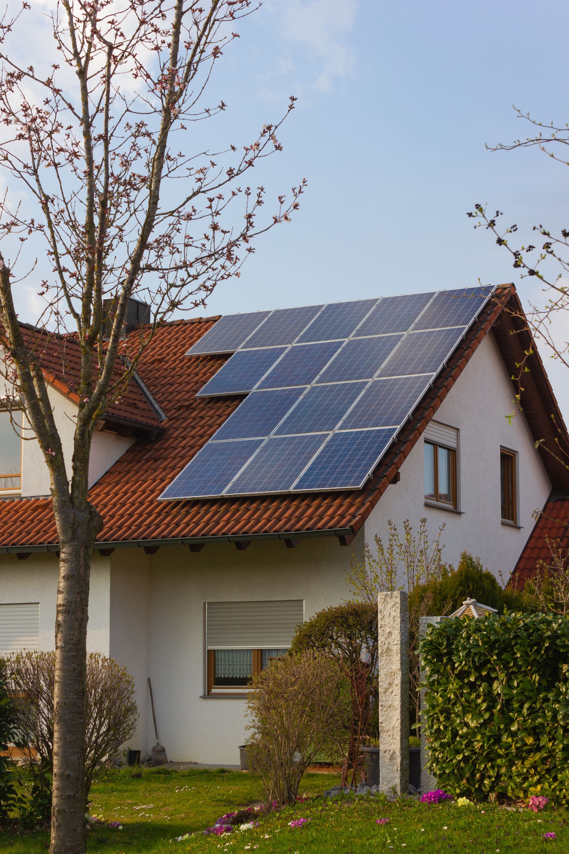 House with red tile roof, solar panels, and a tree on a sunny day.