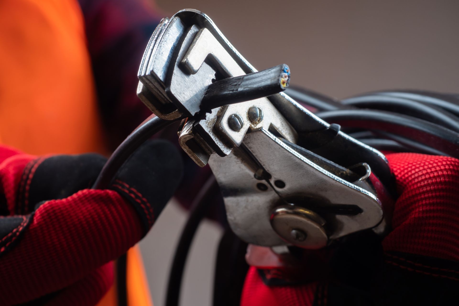 Hands using a ratchet strap to secure black cable, wearing red gloves.